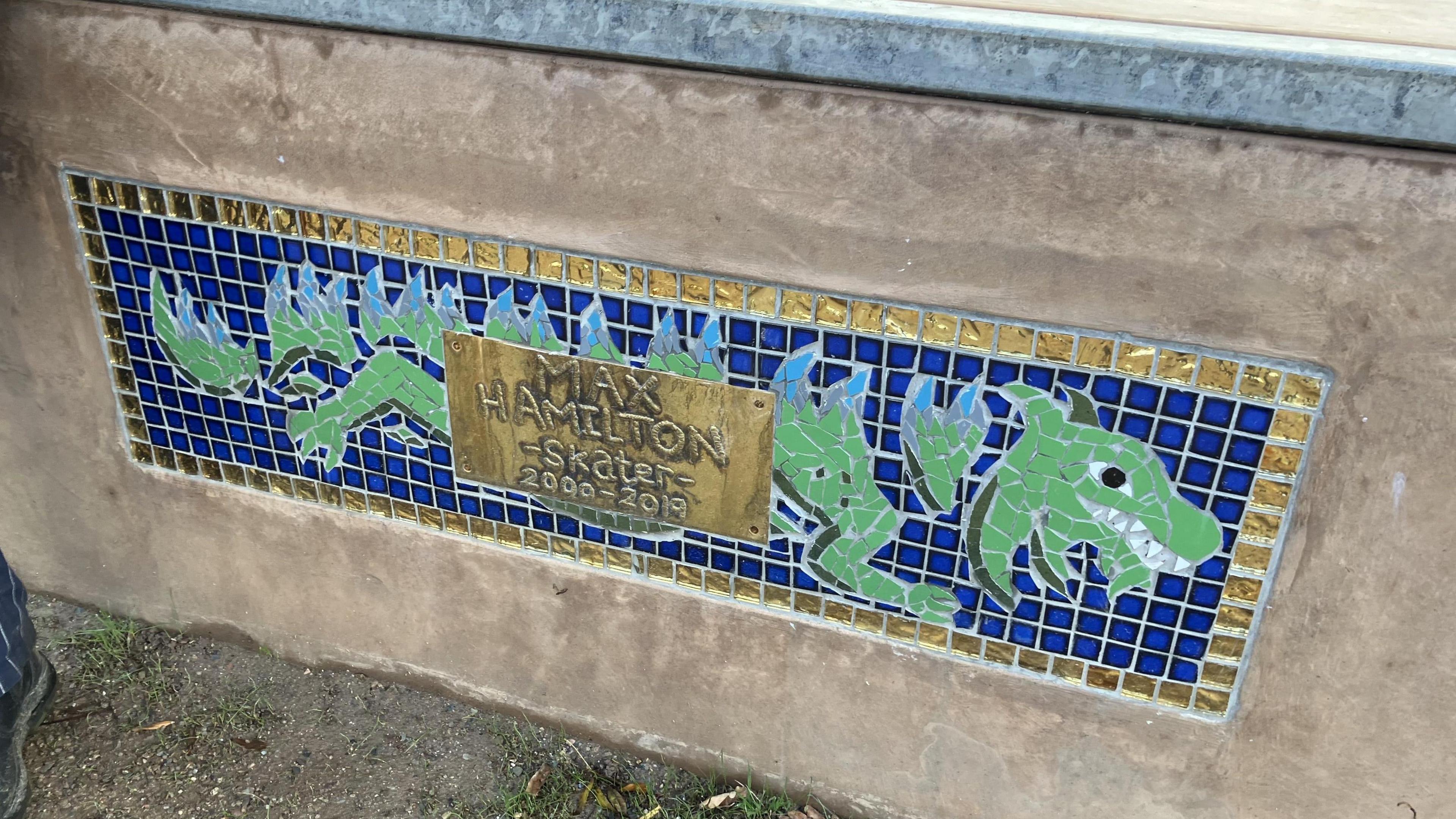 A memorial plaque made from tiles and a metal panel. There is what appears to be a dragon depicted by the tiles, and the metal plaque reads 'Max Hamilton. Skater. 2000-2019.