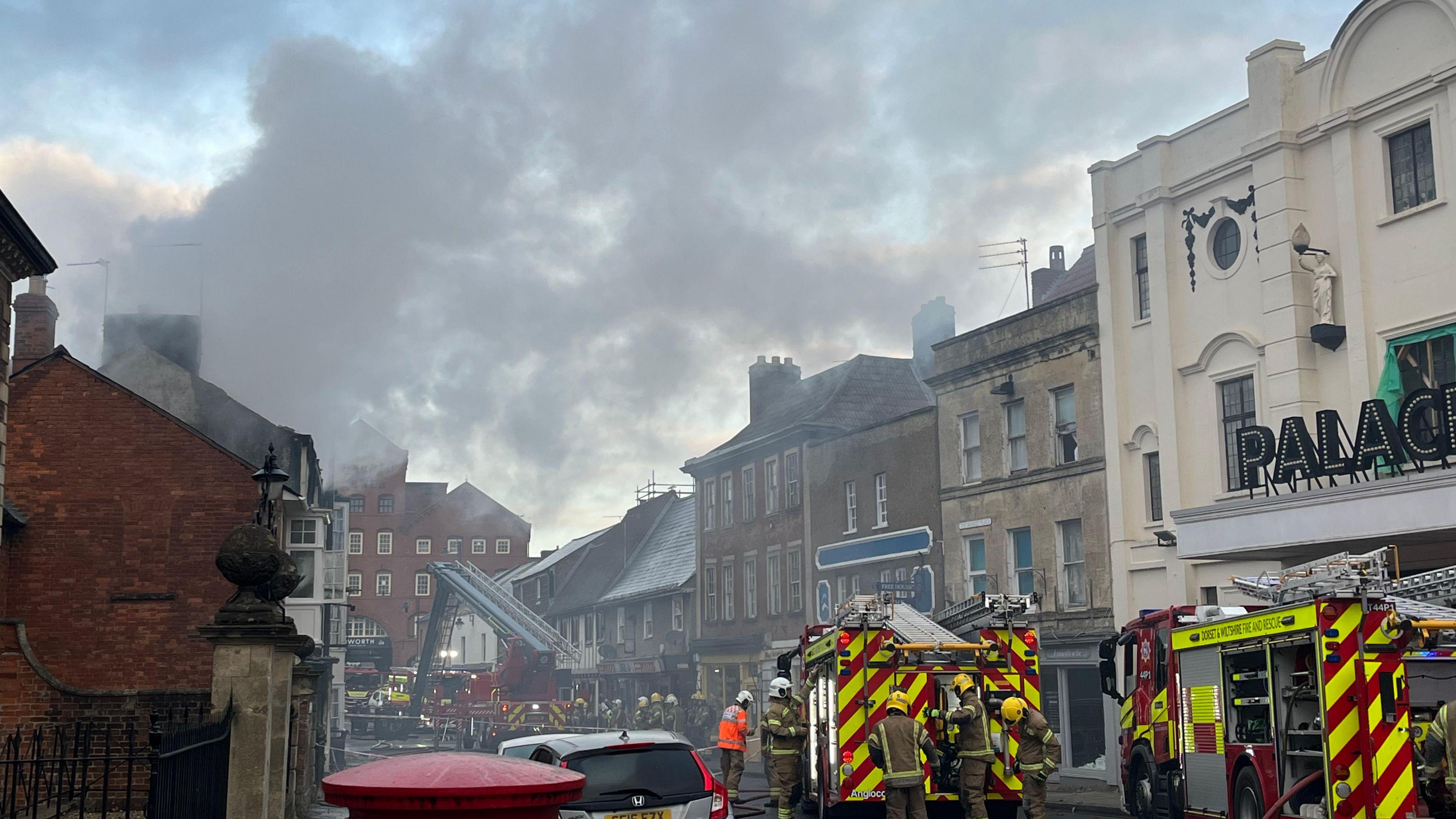 Several fire engines on a road. There is lots of thick smoke in the sky.