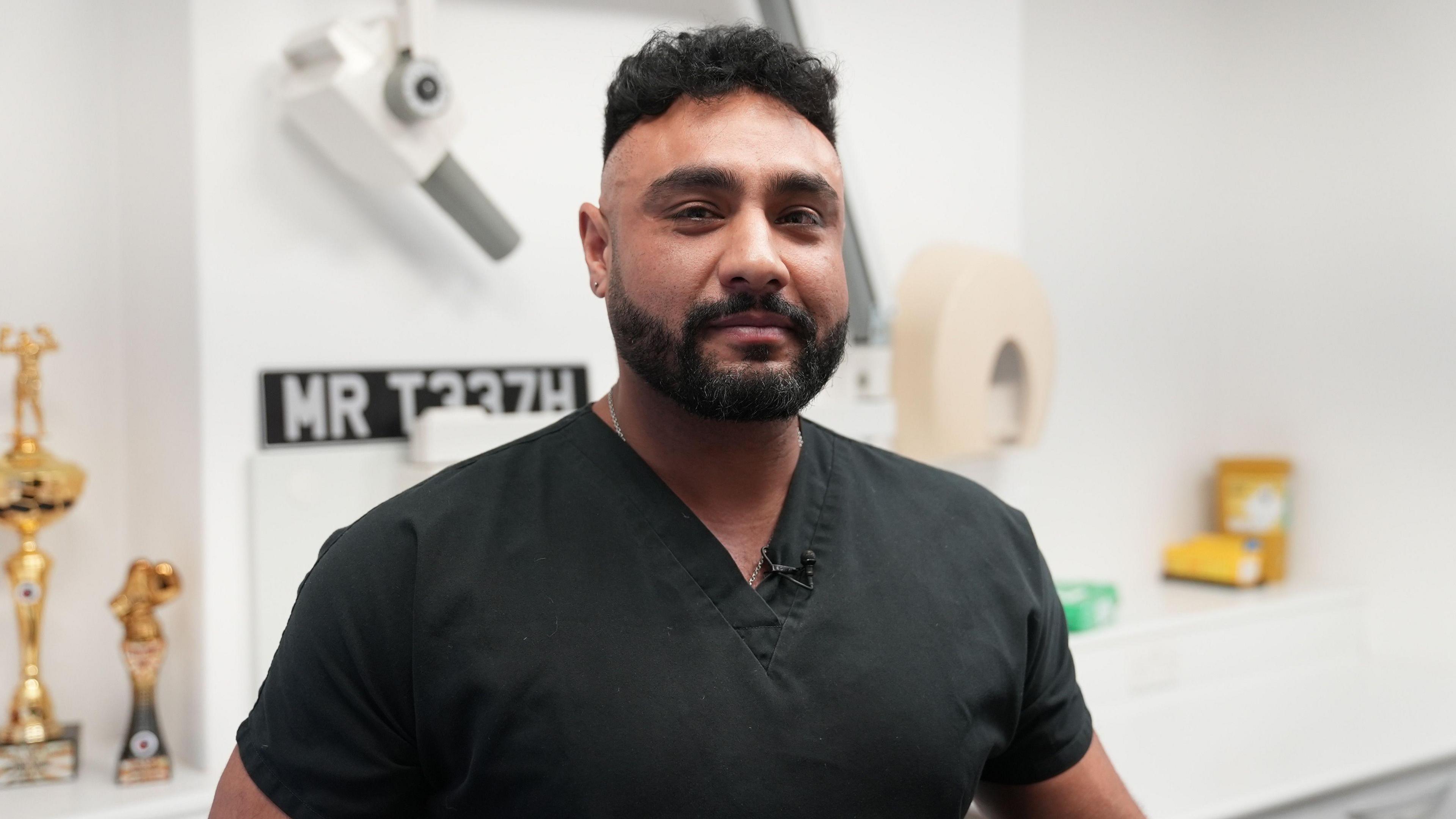 Dr Harj Singrao in his dentist scrubs is stood in his clinic looking at the camera