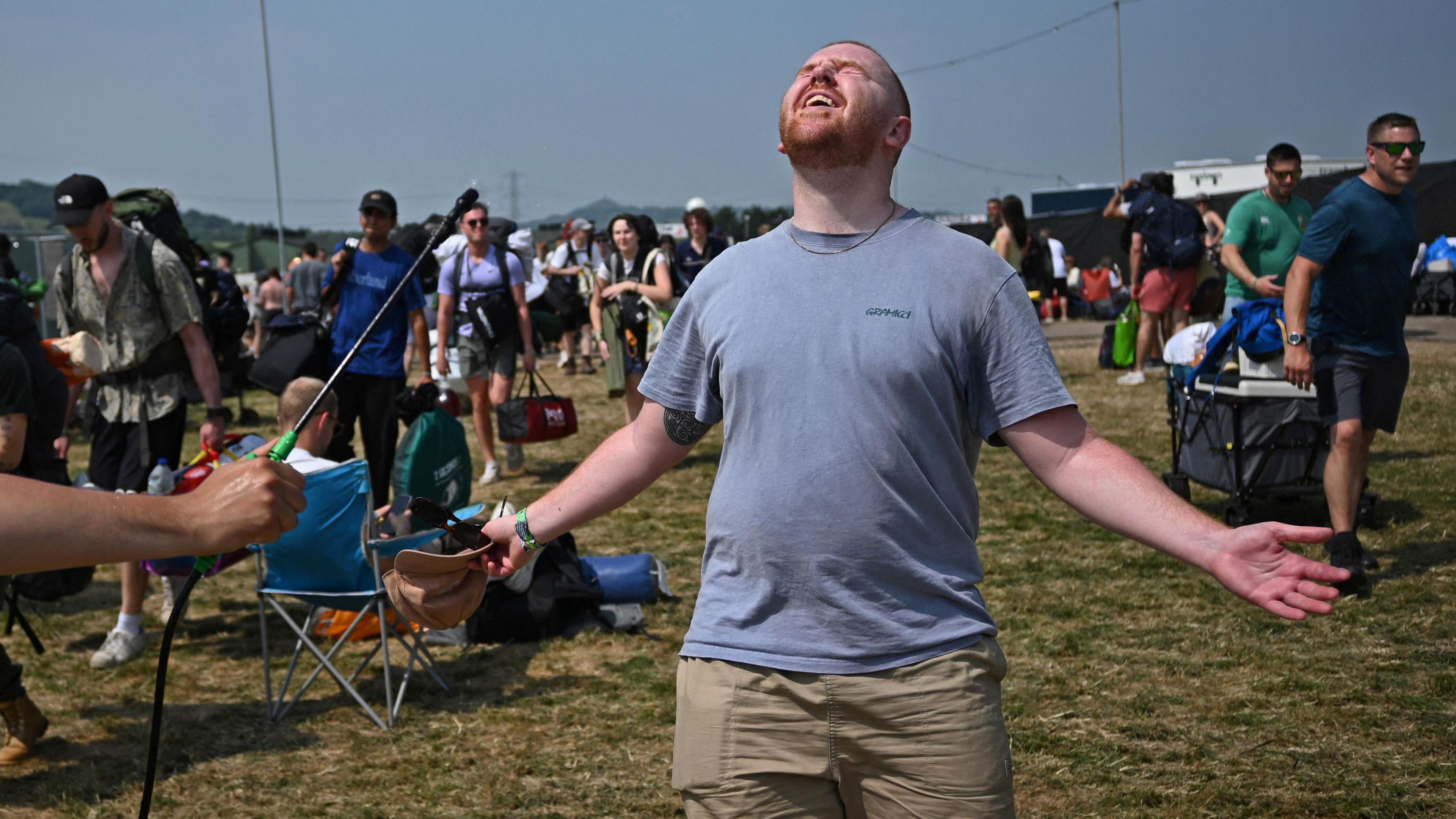 Man in a grey T-shirt with his arms outstretched and head back as he is hosed down in a field