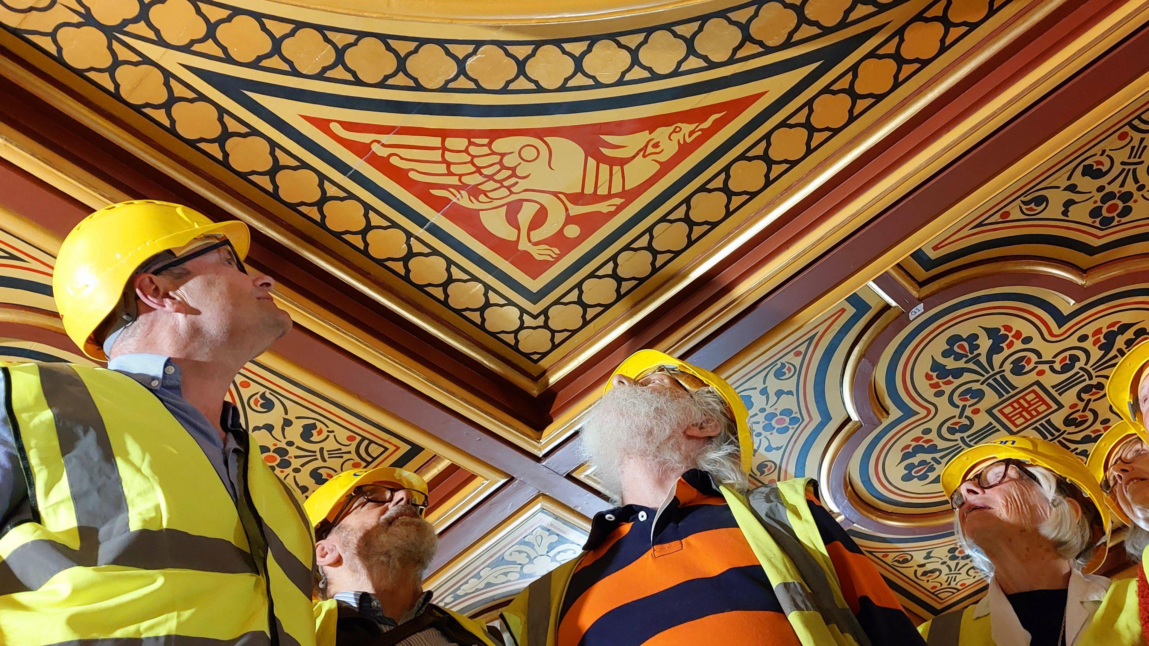 People in hard hats looking at a ceiling with a dragon design.