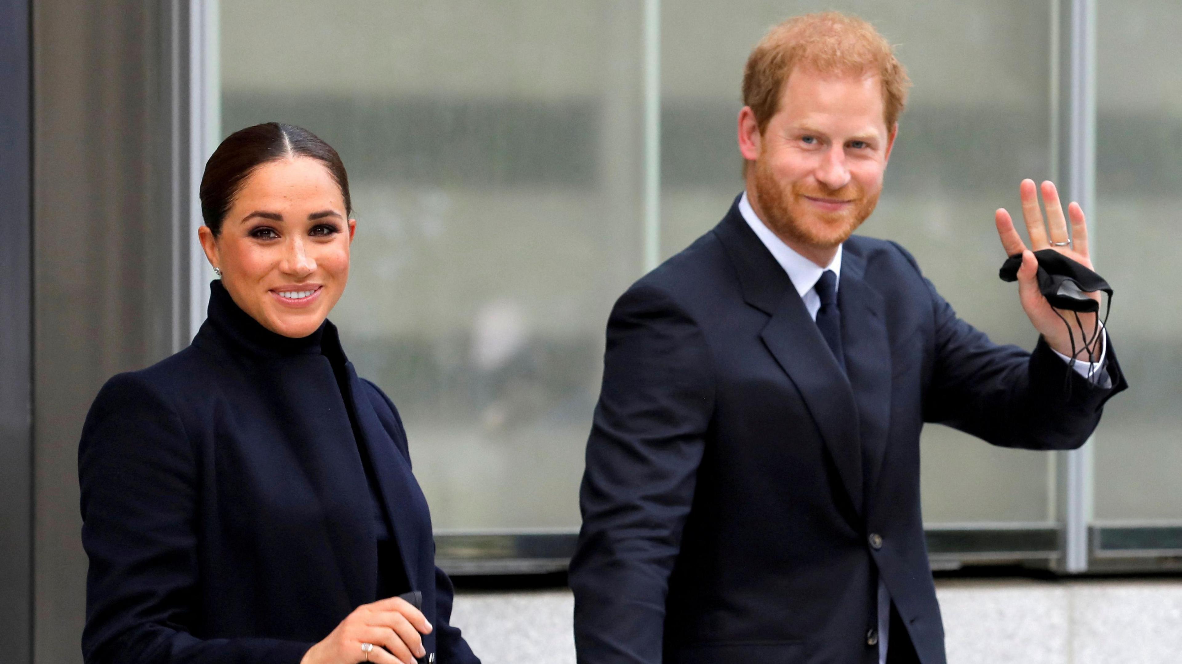 Prince Harry and Meghan, Duke and Duchess of Sussex, wave and smile at the camera.