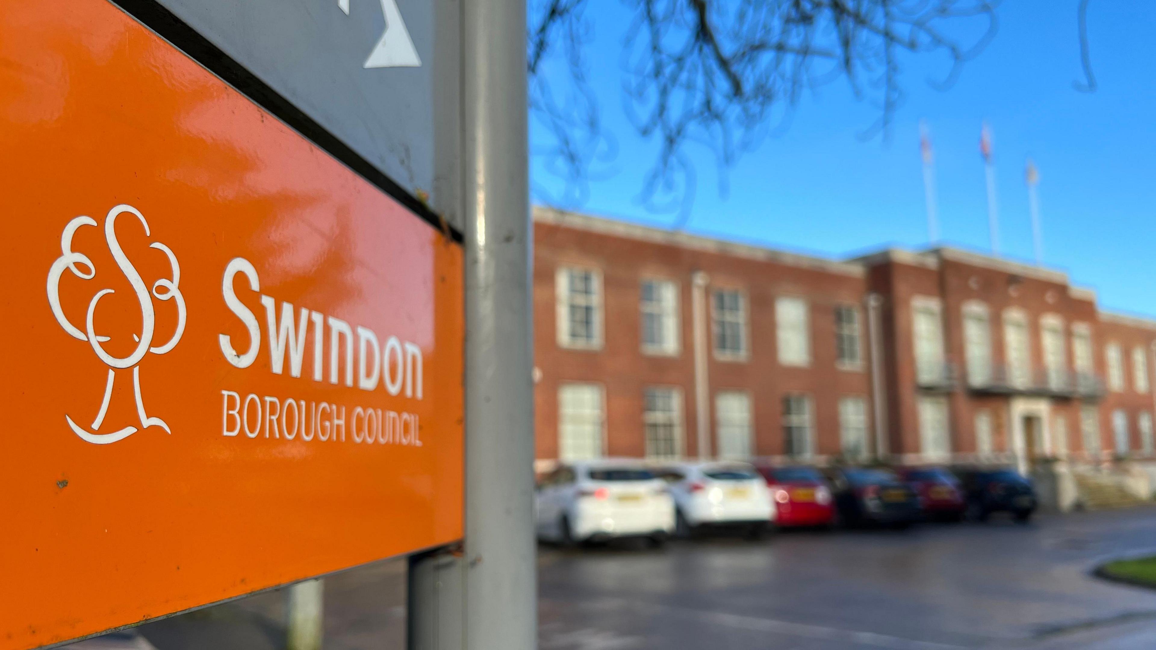 Part of an orange Swindon Borough Council sign with the HQ in the background