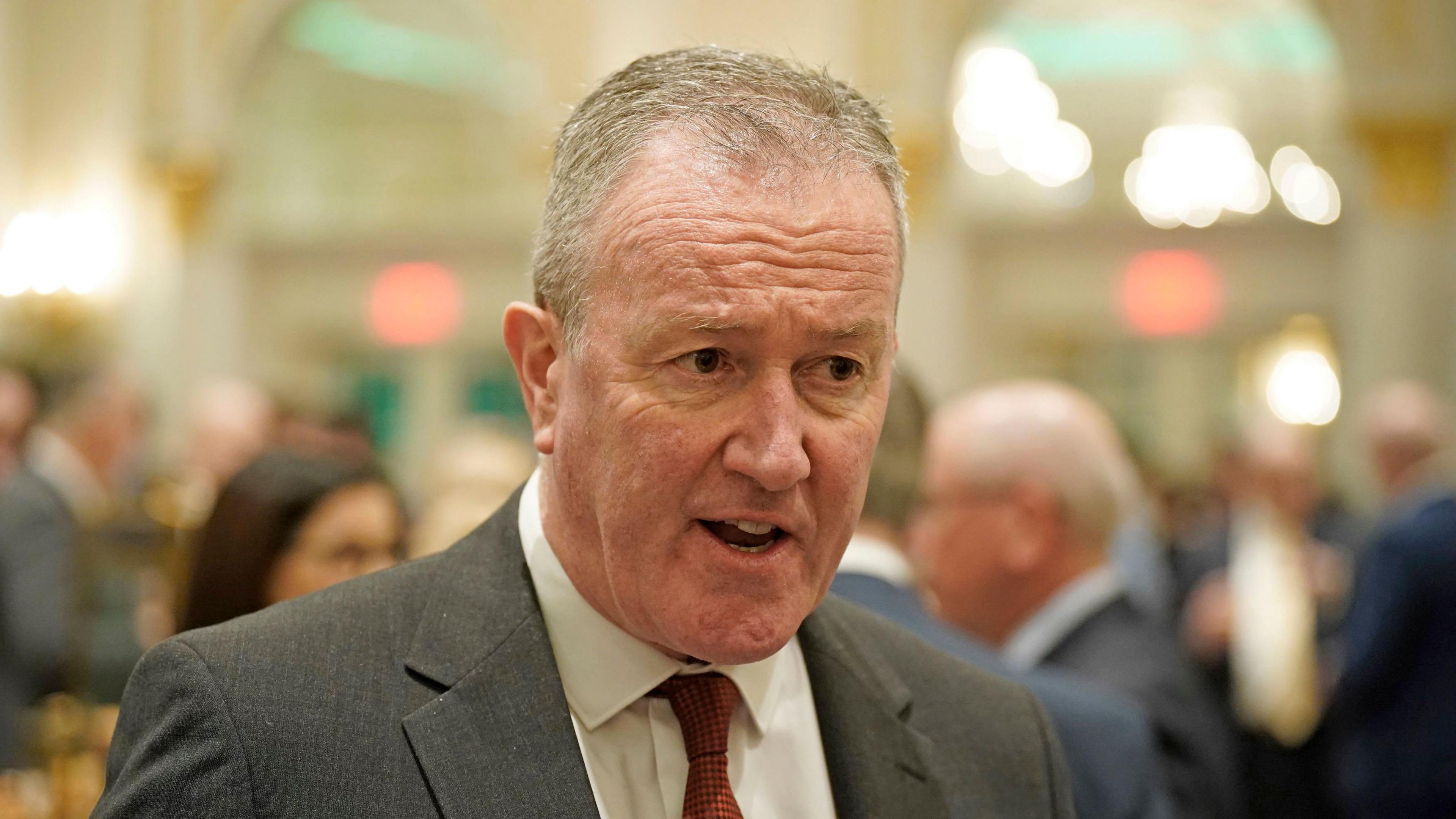 Conor Murphy wearing a grey suit, white shirt and orange tie