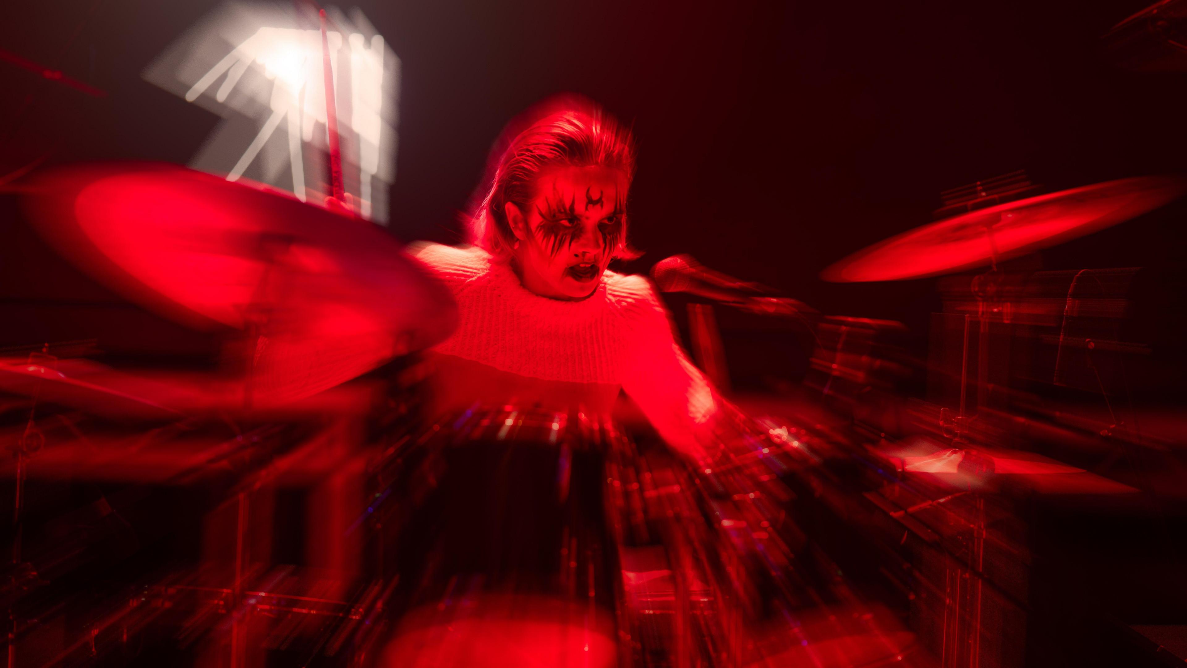 Drummer of Witch Club Satan with satanic make-up is drenched in red light. 