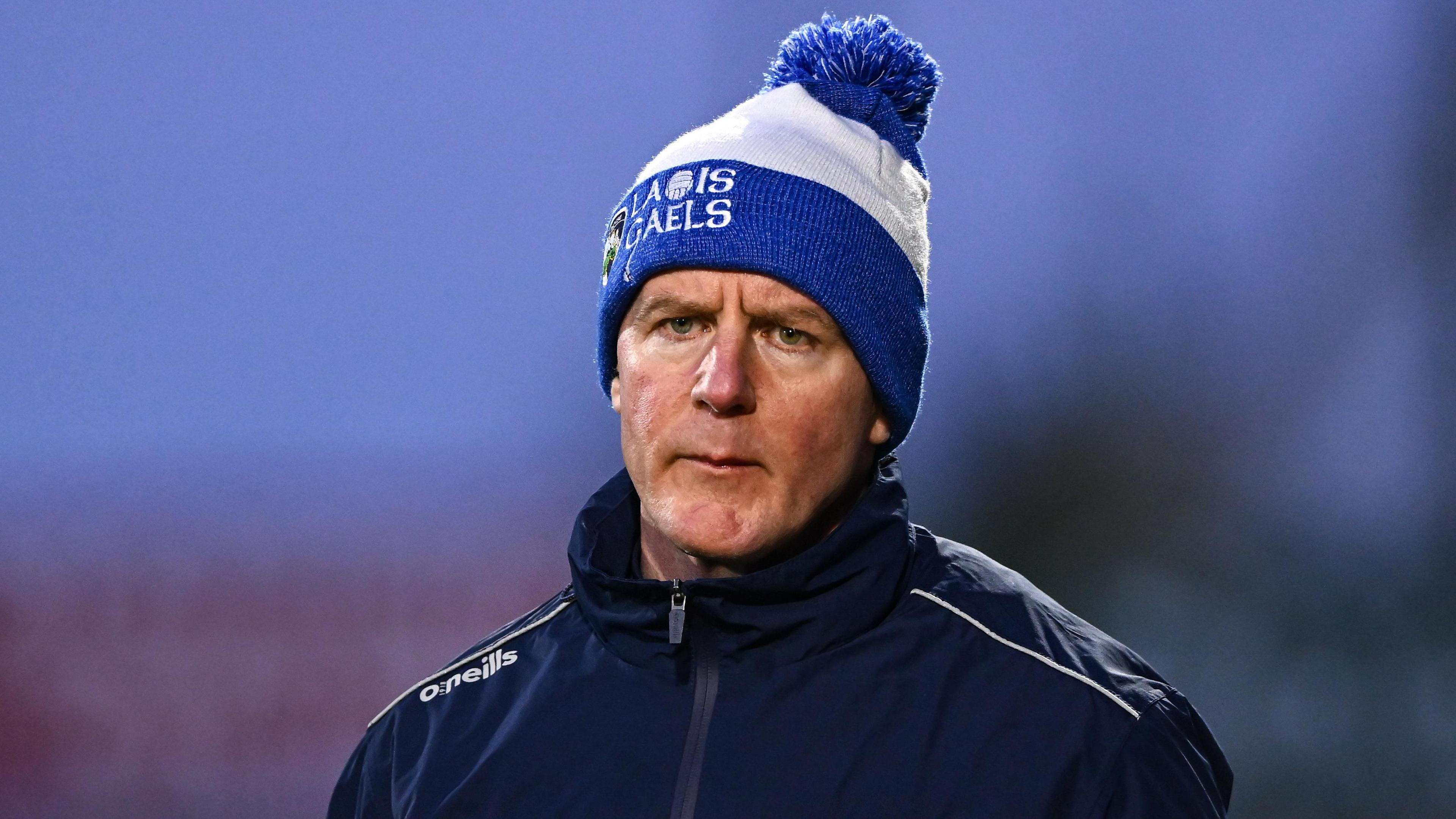 Justin McNulty - a man wearing a white and blue beanie hat that says 'Laois Gaels' and a dark zip jacket