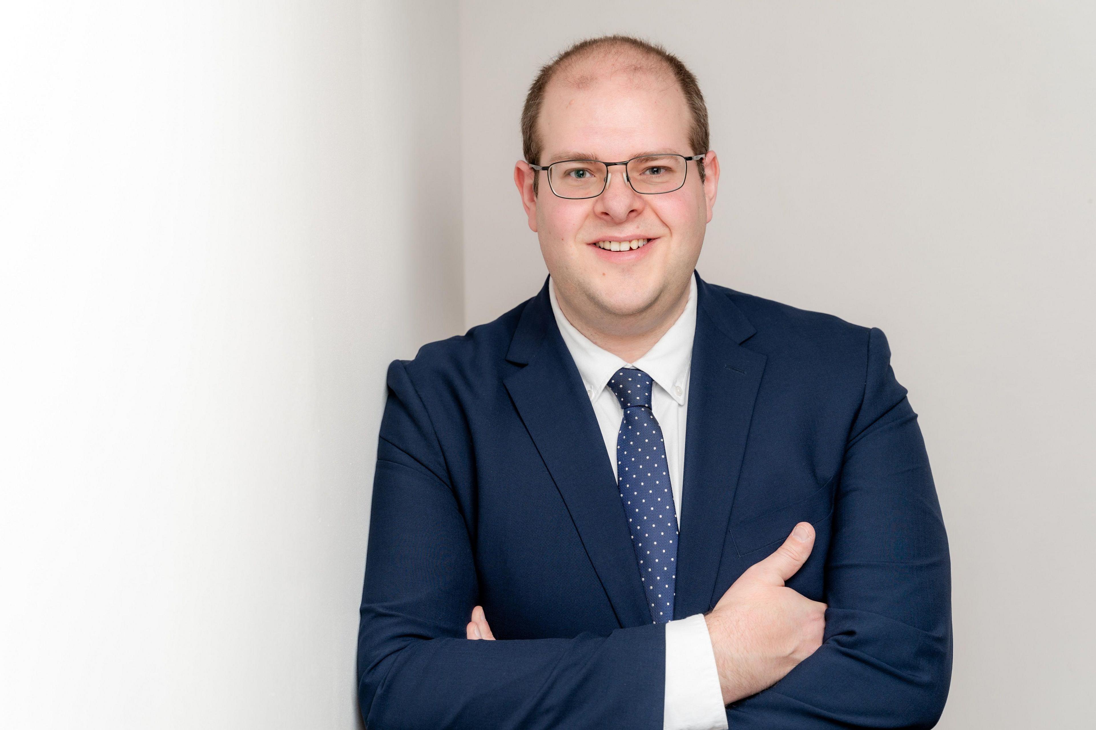 Conservative candidate Jonathan Ash-Edwards in a navy blue suit and tie, wearing glasses