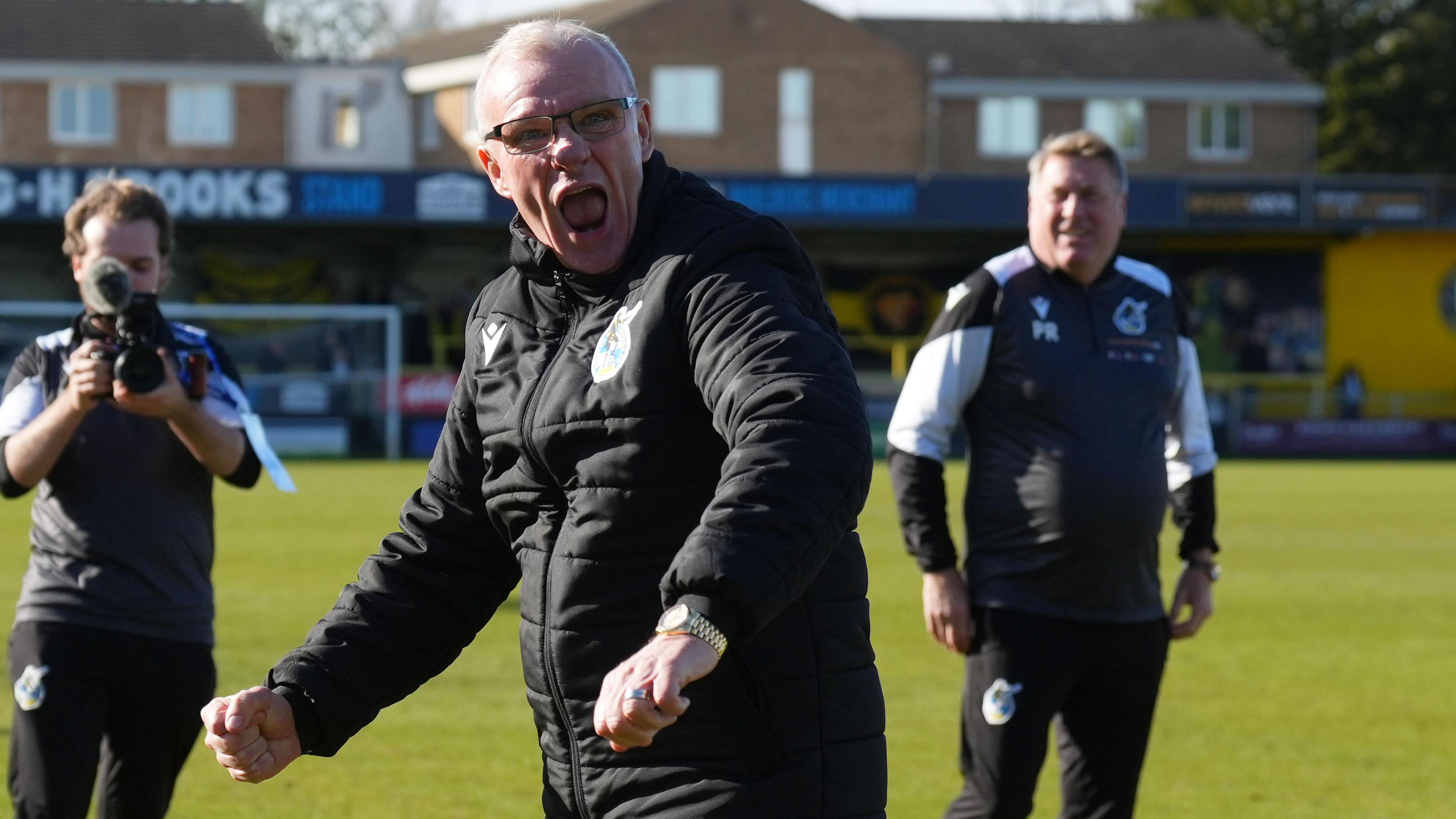 Steve Evans clenches his fists and shouts with his mouth open while walking on the pitch at the end of Bristol Rovers' win against Harrogate