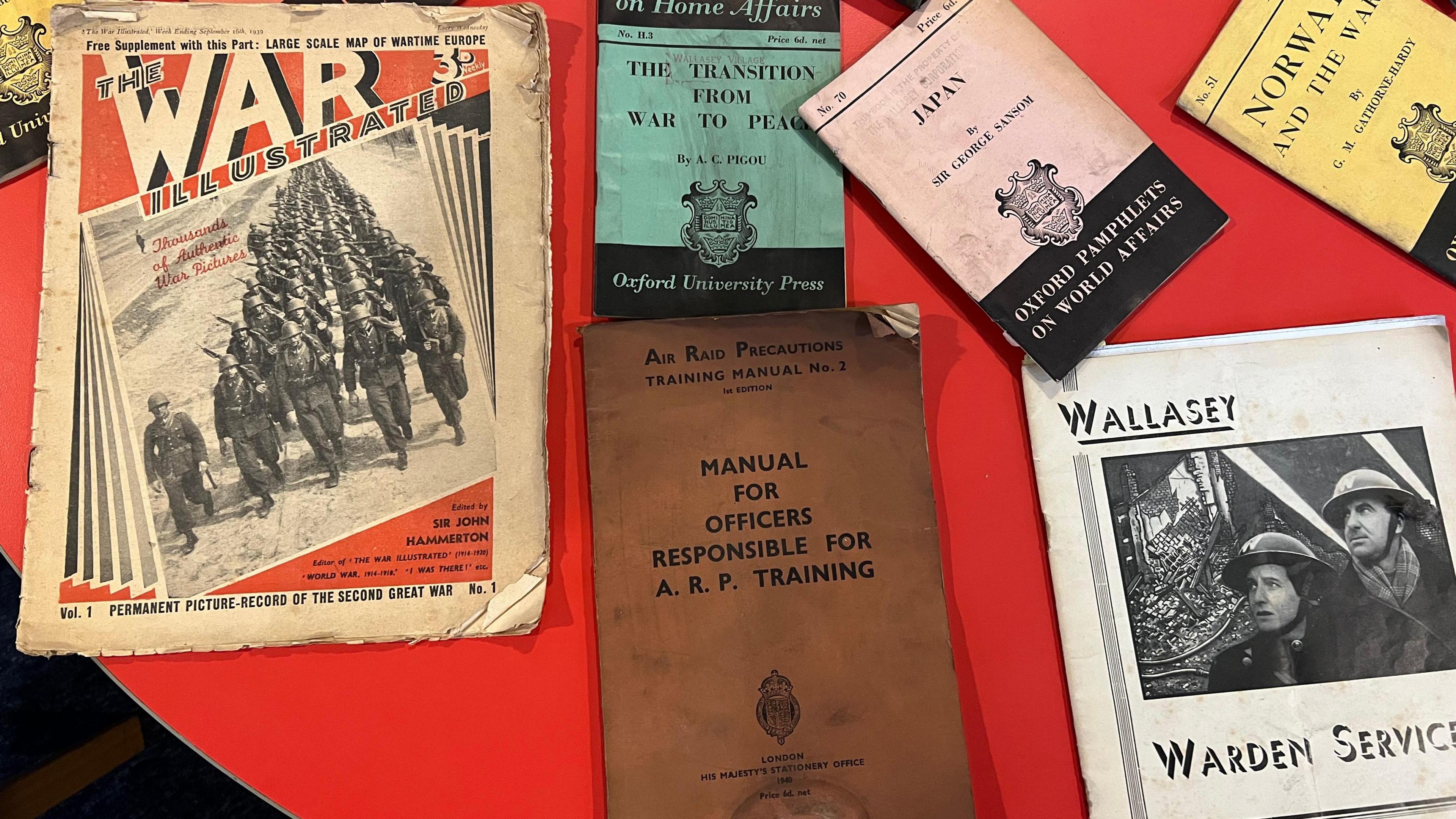 Various leaflets on a red table, with some dating back may years discussing the war 