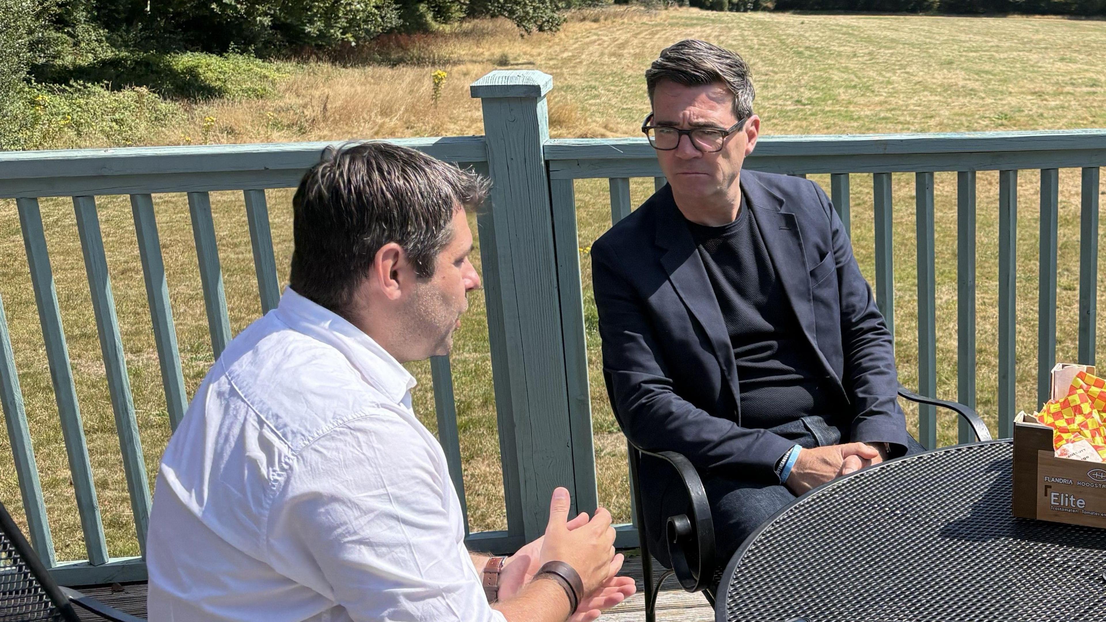 Andy Burnham wearing a dark top and jacket sitting next to Leigh Frost on his recent visit to Cornwall