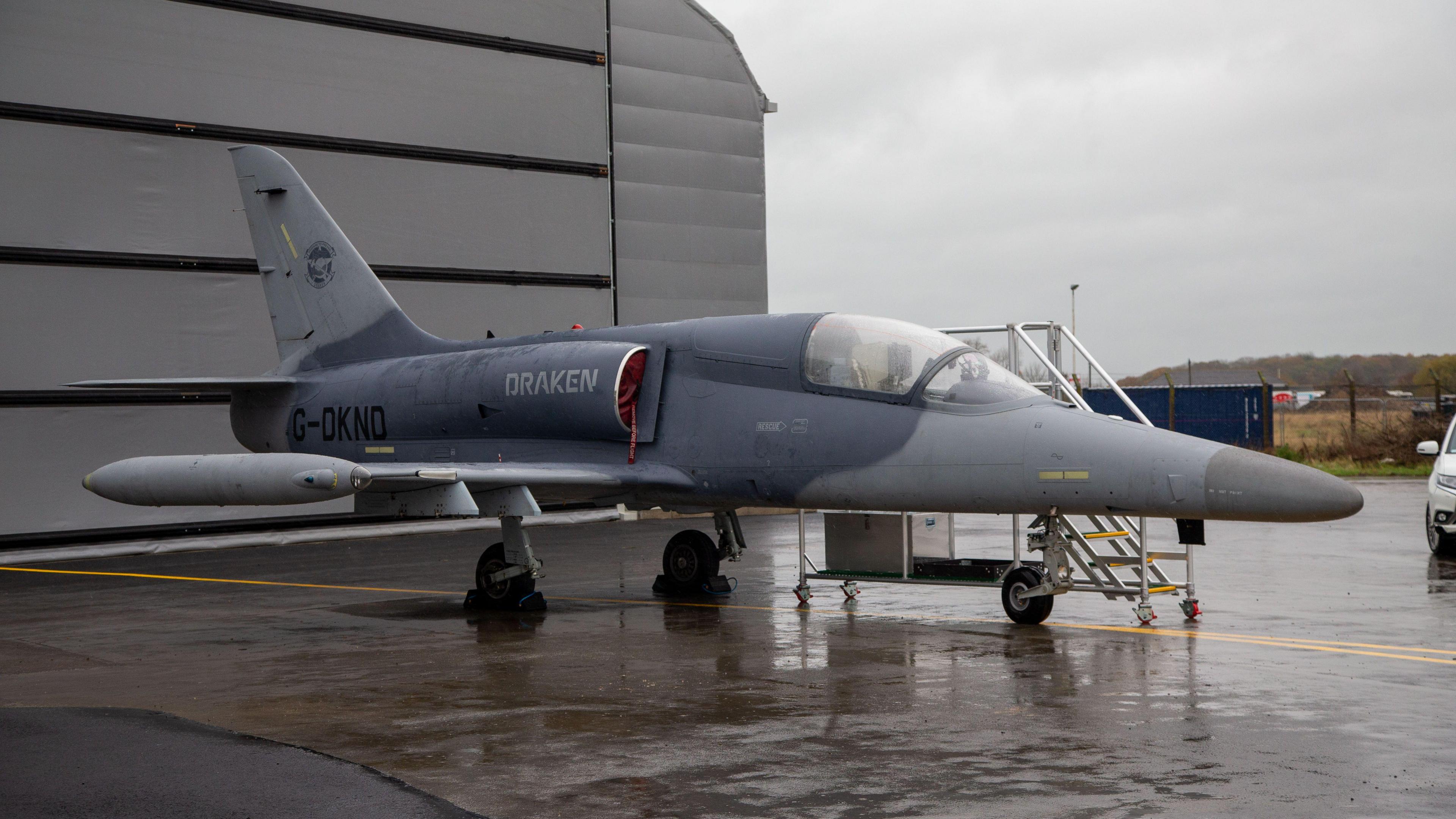 A Draken fighter jet parked outside a hangar at Teesside Airport. The grey aircraft has a long nose and a small cockpit. 