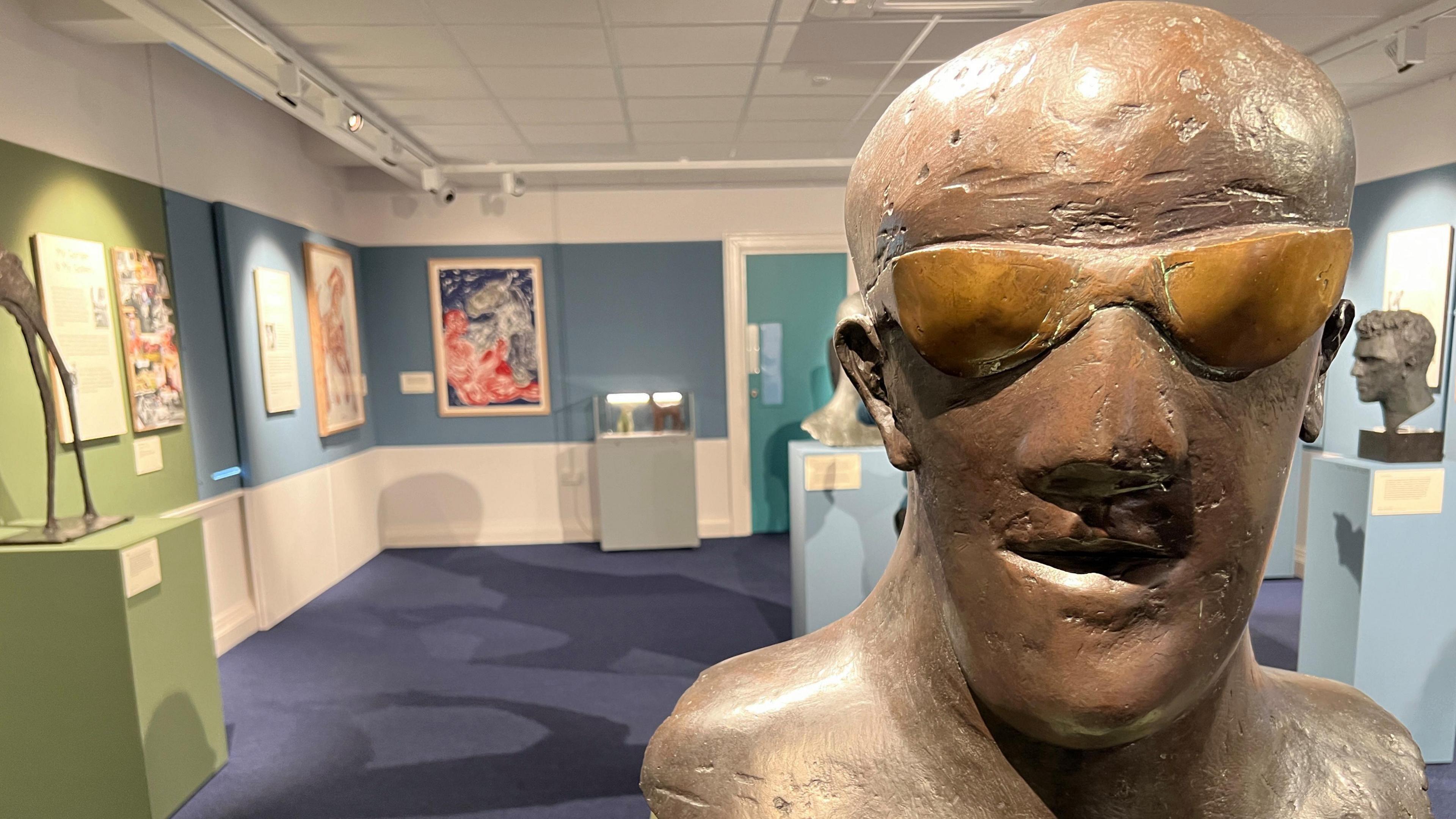 A bronze bust sculpture of a man inside the Swindon museum, with blue carpets and walls.