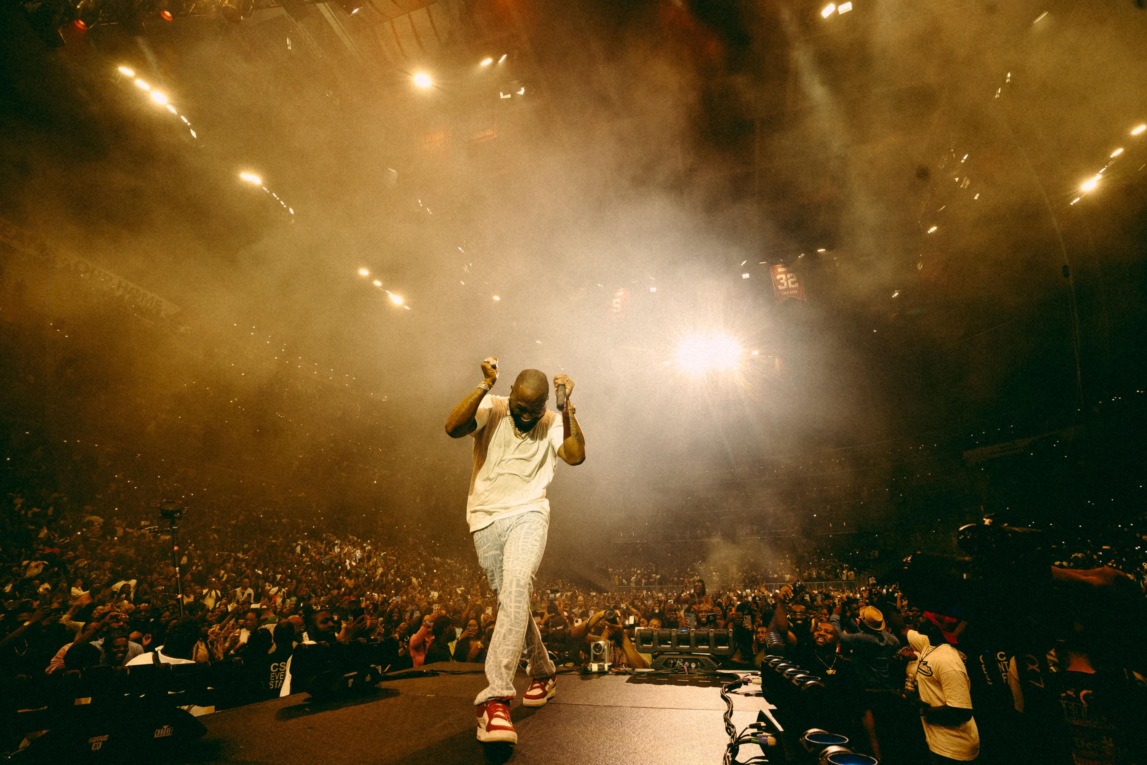 David dressed in a white T-shirt, light jeans and red and white shoes holds up his fists (microphone in one) with his back to a huge audience as he perform at the Capital One Arena in Washington DC - 1 July 2023.