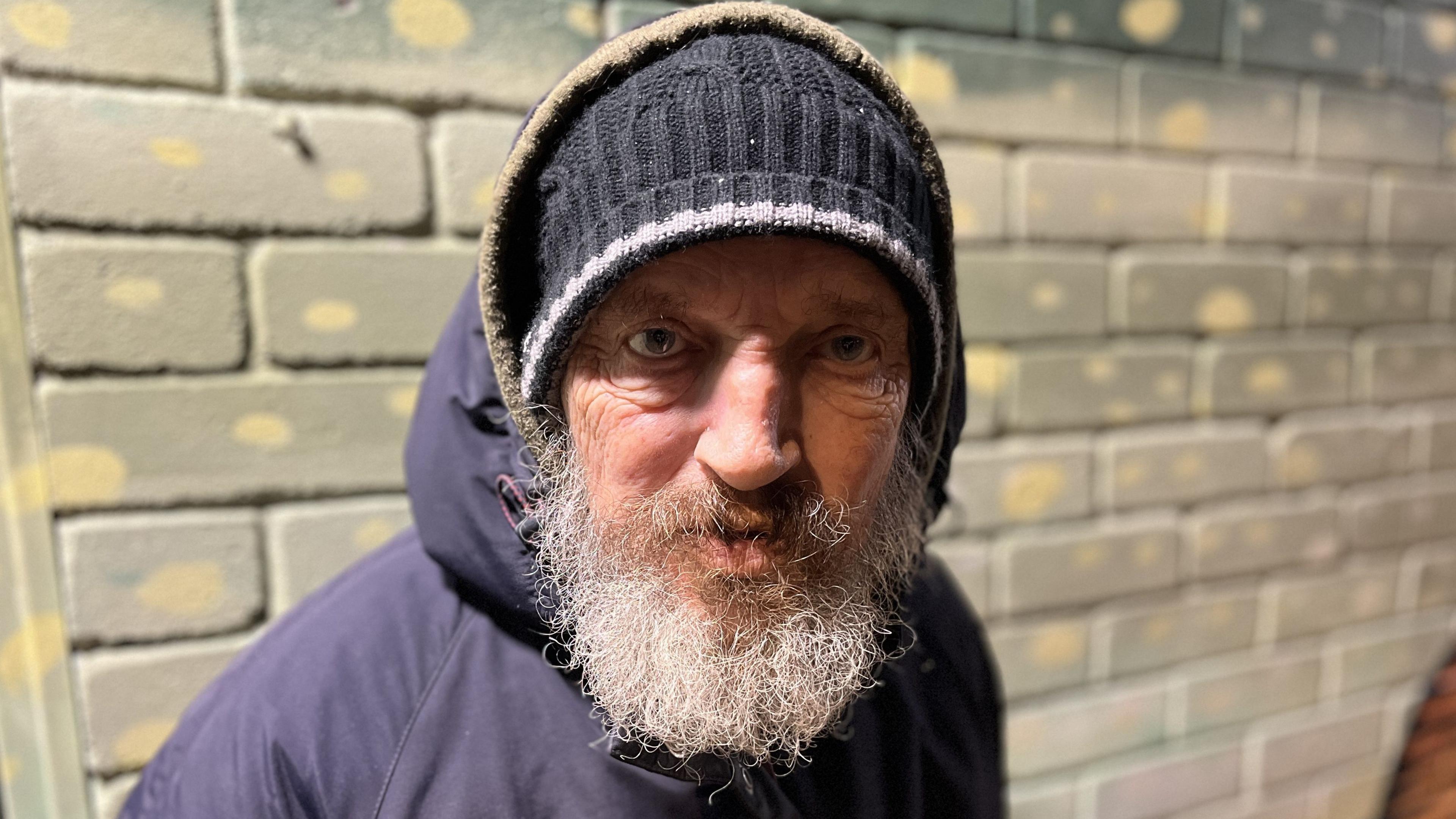 Service user Shaun wearing a navy blue beanie hat with his hood up and large grey beard