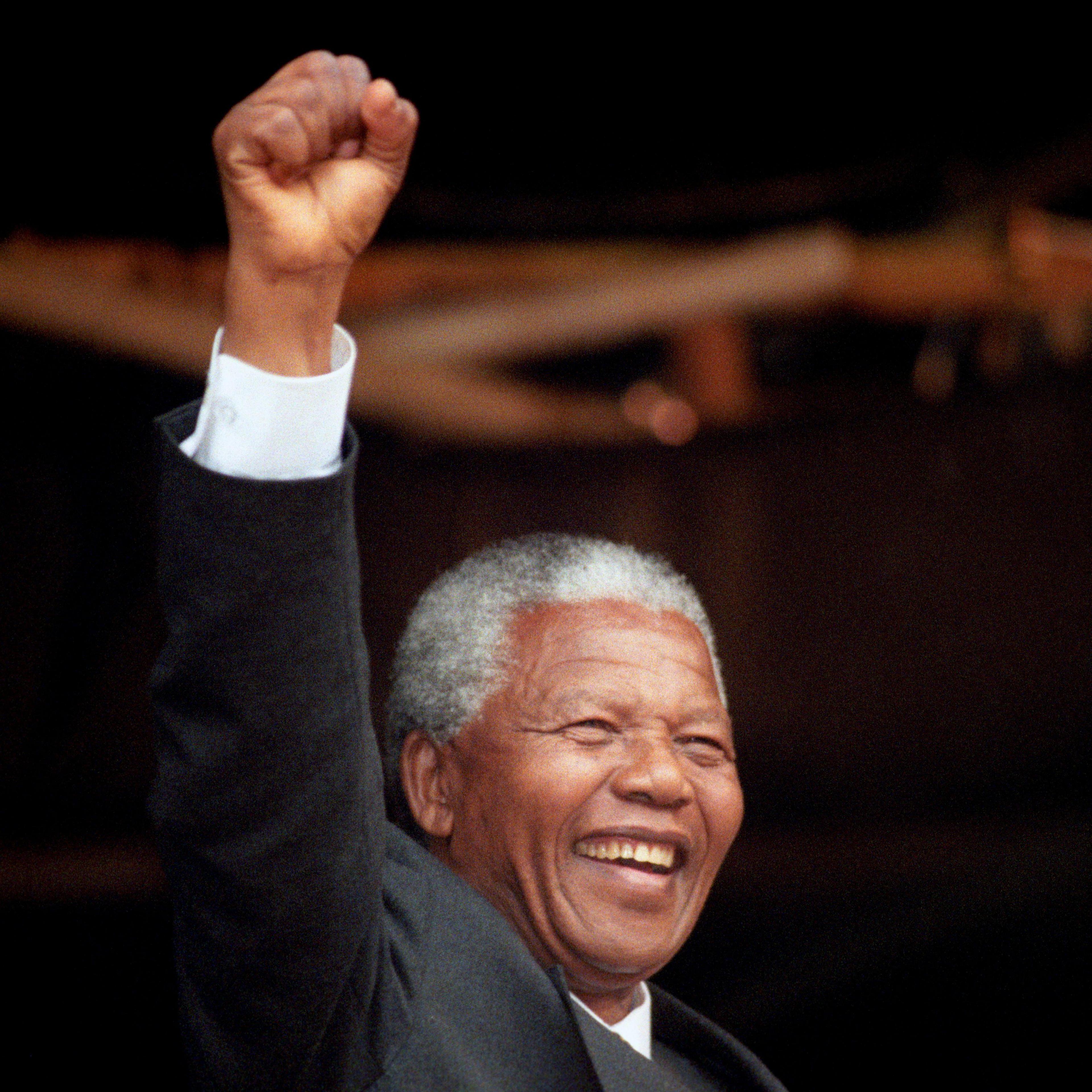 A man with white hair, punching the air while standing on a stage outdoors