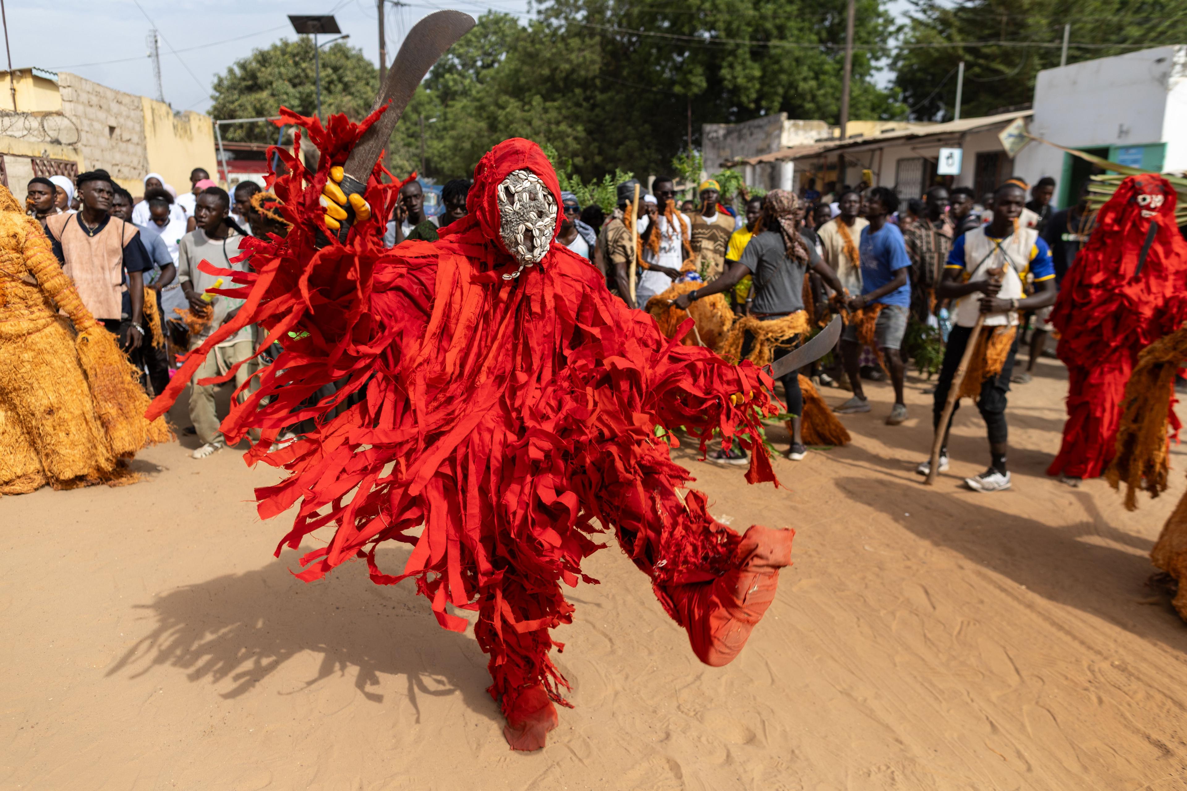 People dressed in red, tasselled costumes dance as a part of a masquerade.
