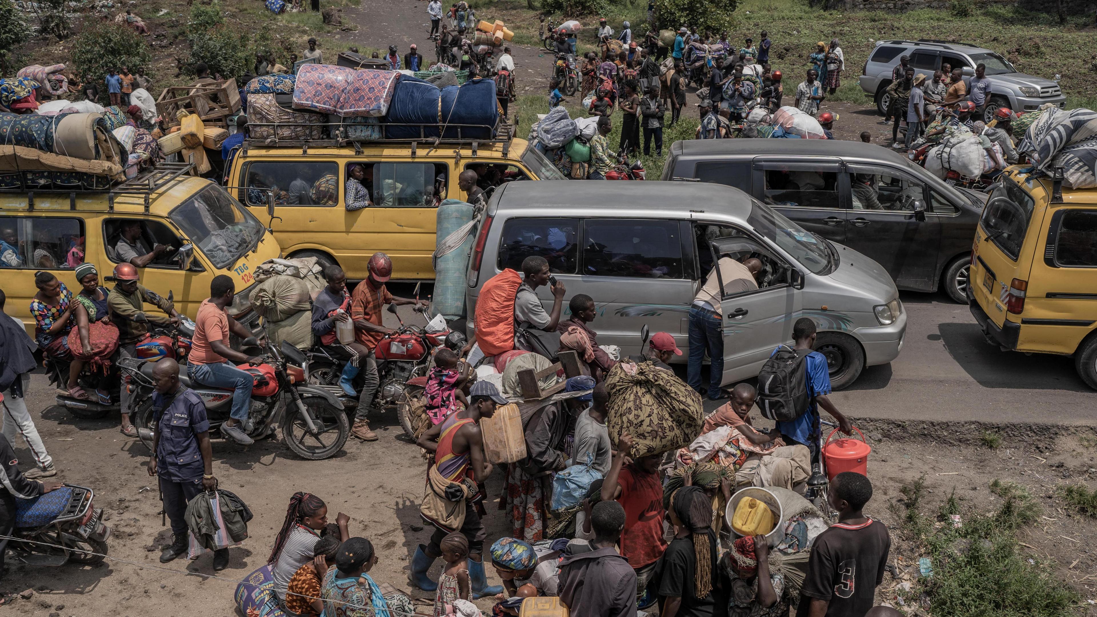 People gather at a busy road while carrying some of their belongings as they flee the Masisi territory following clashes between M23 rebels and government forces, at a road near Sake, DR Congo - February 2024