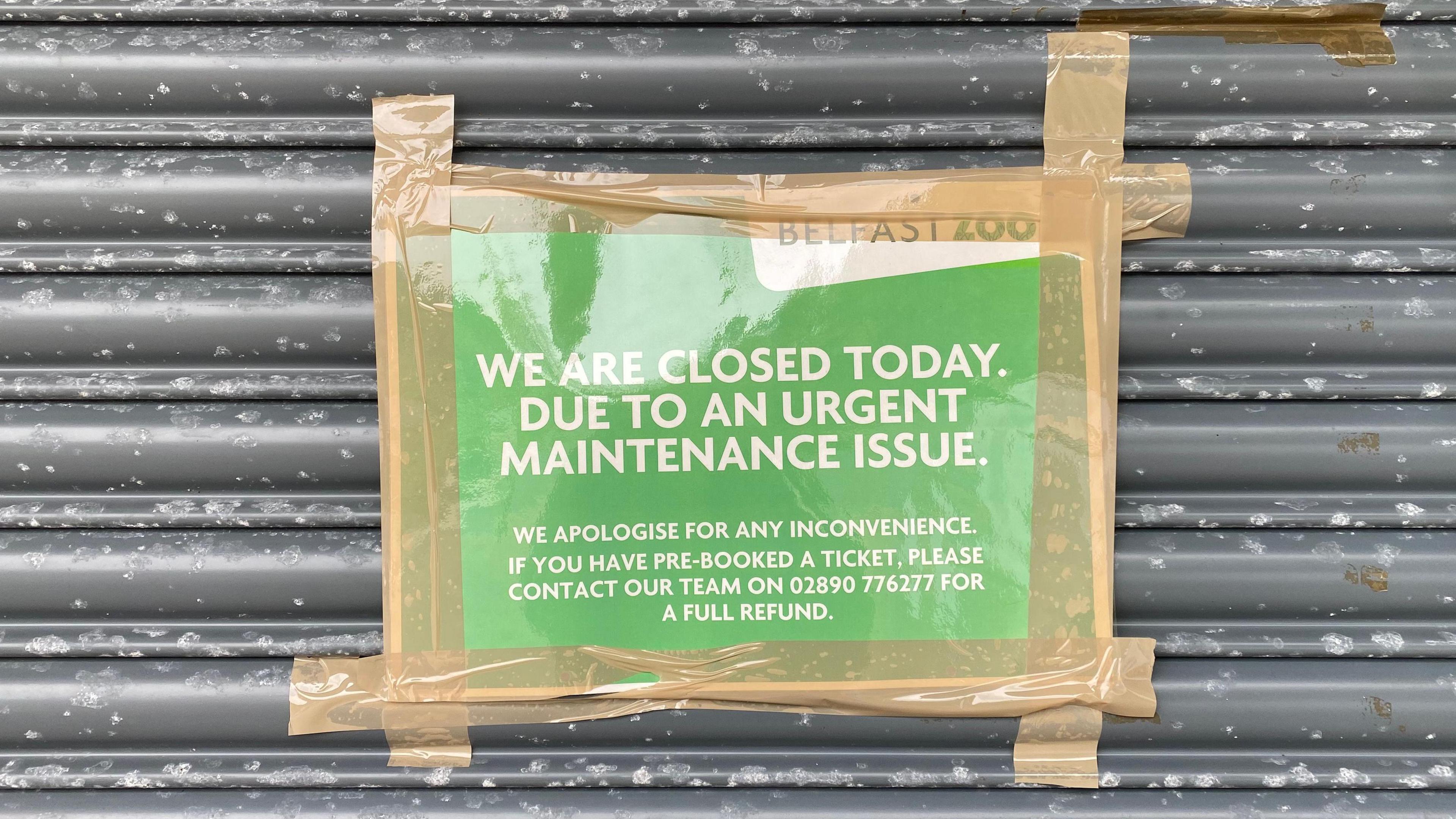 A green sign with white text is taped to a grey door. The tape is brown.