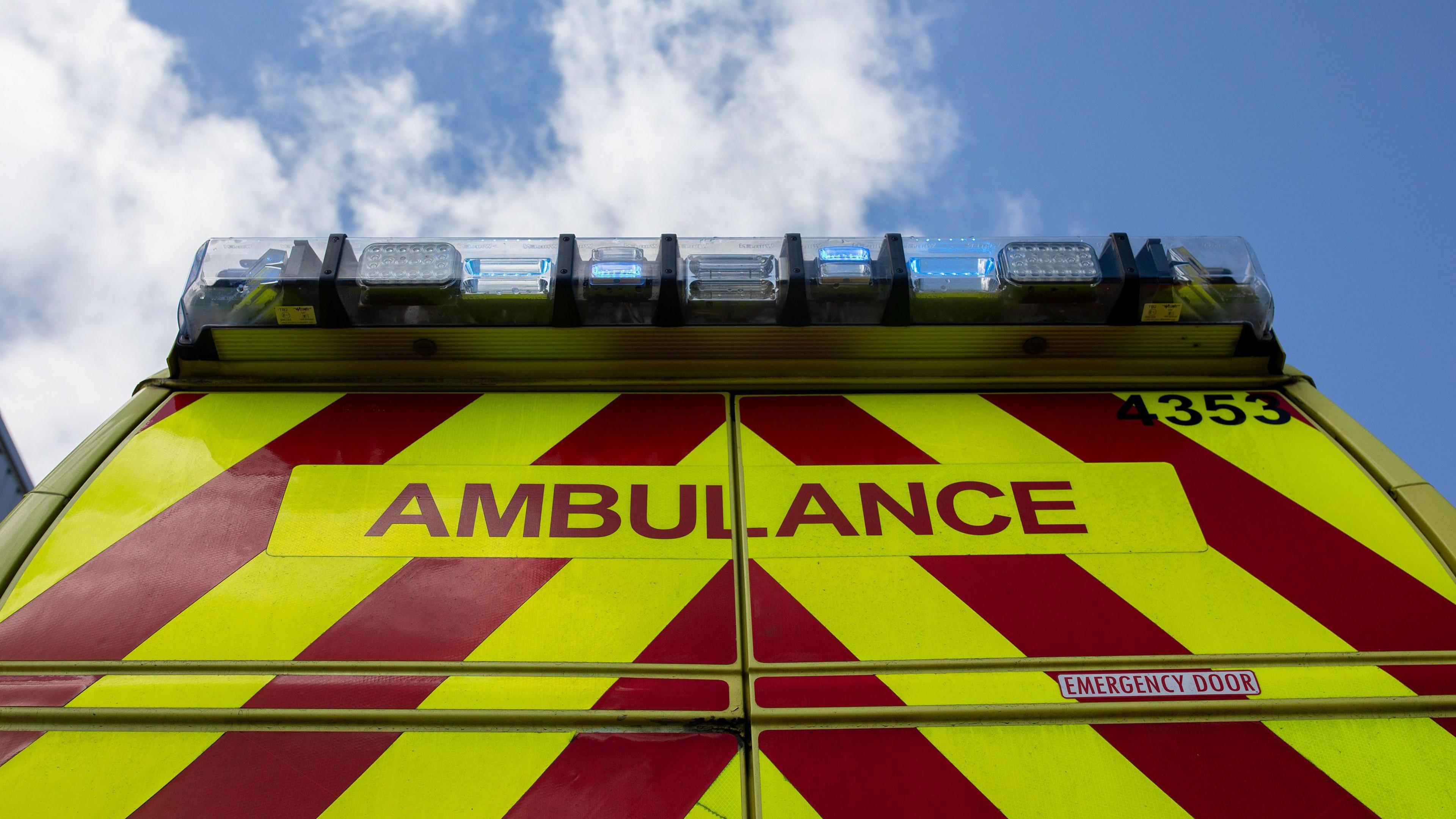 A stock image of an ambulance shown from the back with the blue lights on