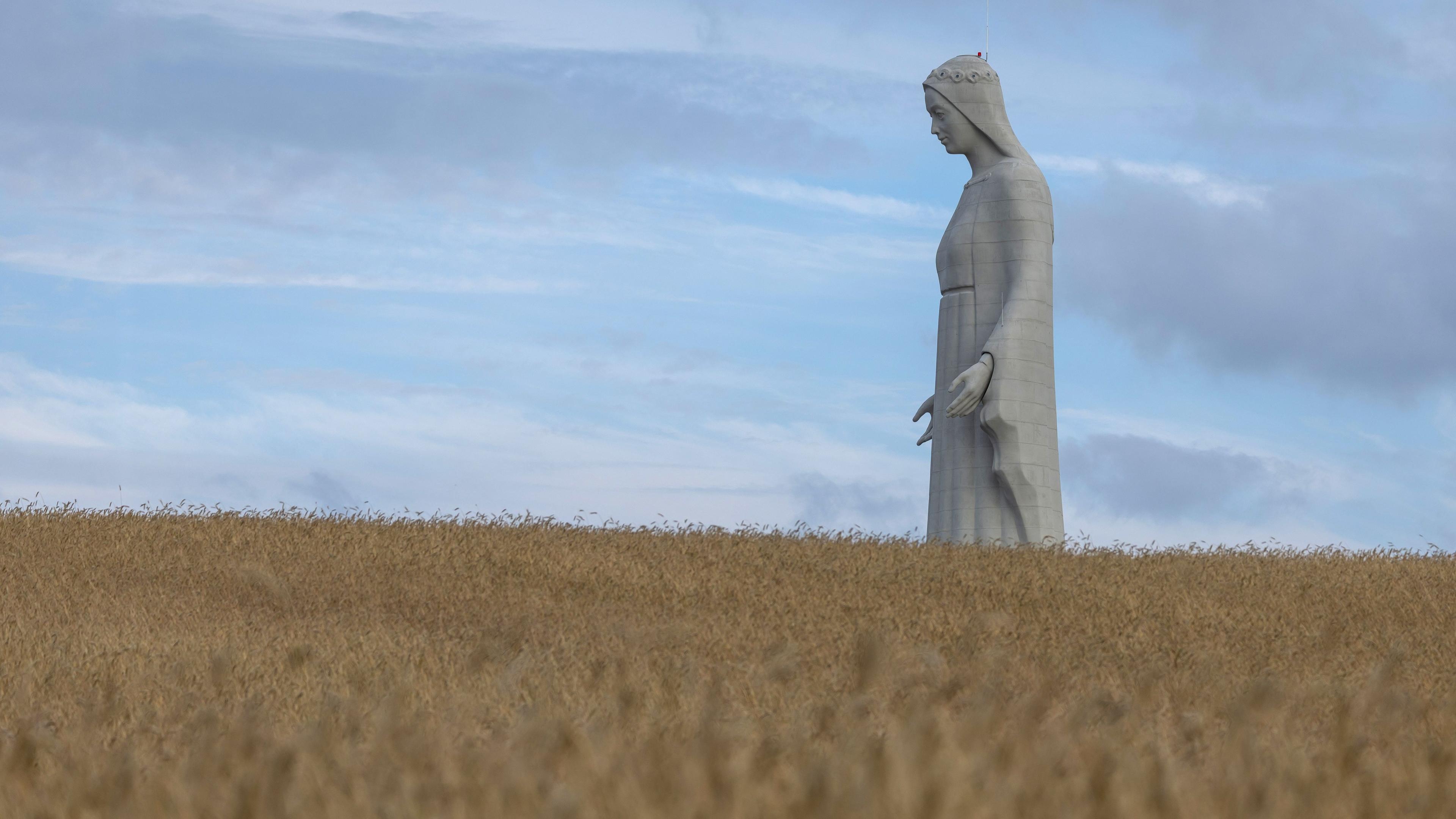 A statue of the Virgin Mary rises above a wheat field.