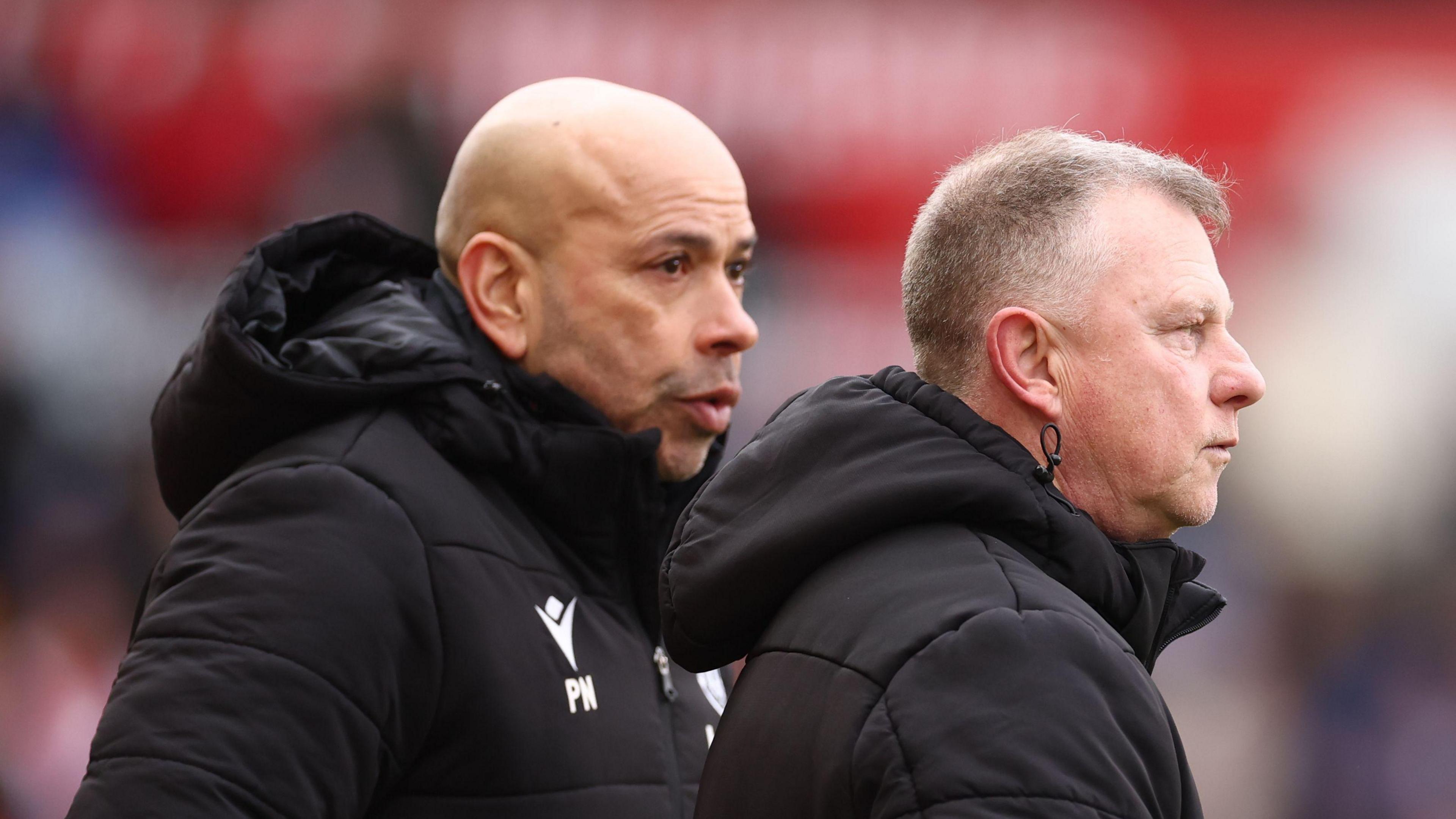 Paul Nevin standing just behind head coach Mark Robins on the touchline 