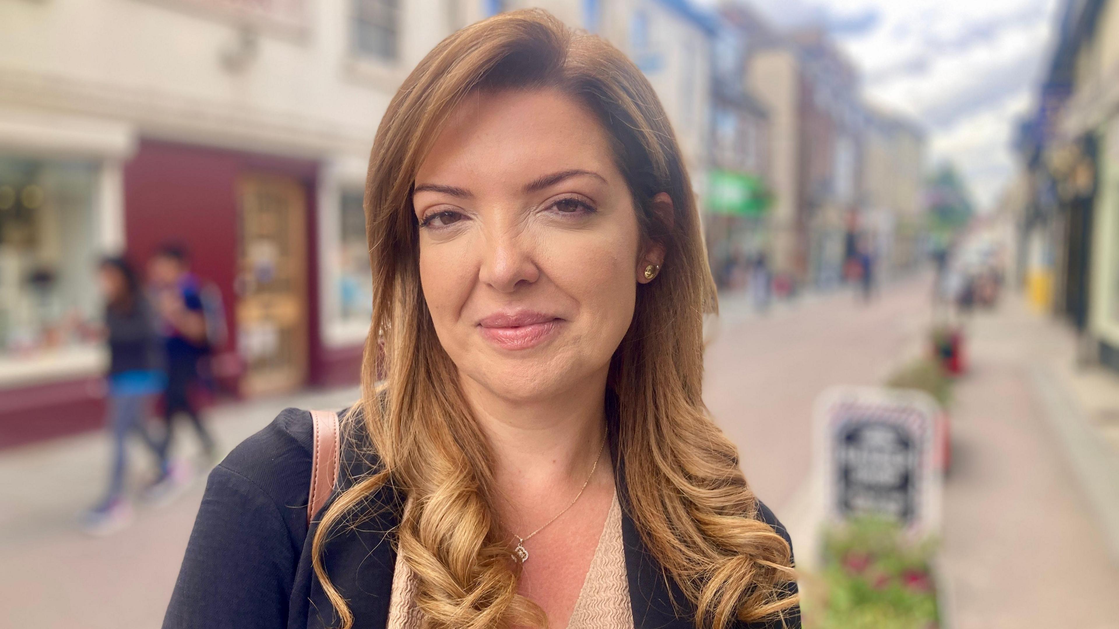 Woman with long strawberry auburn hair stares into camera. She's wearing a navy blue jacket with Royston town centre in the background