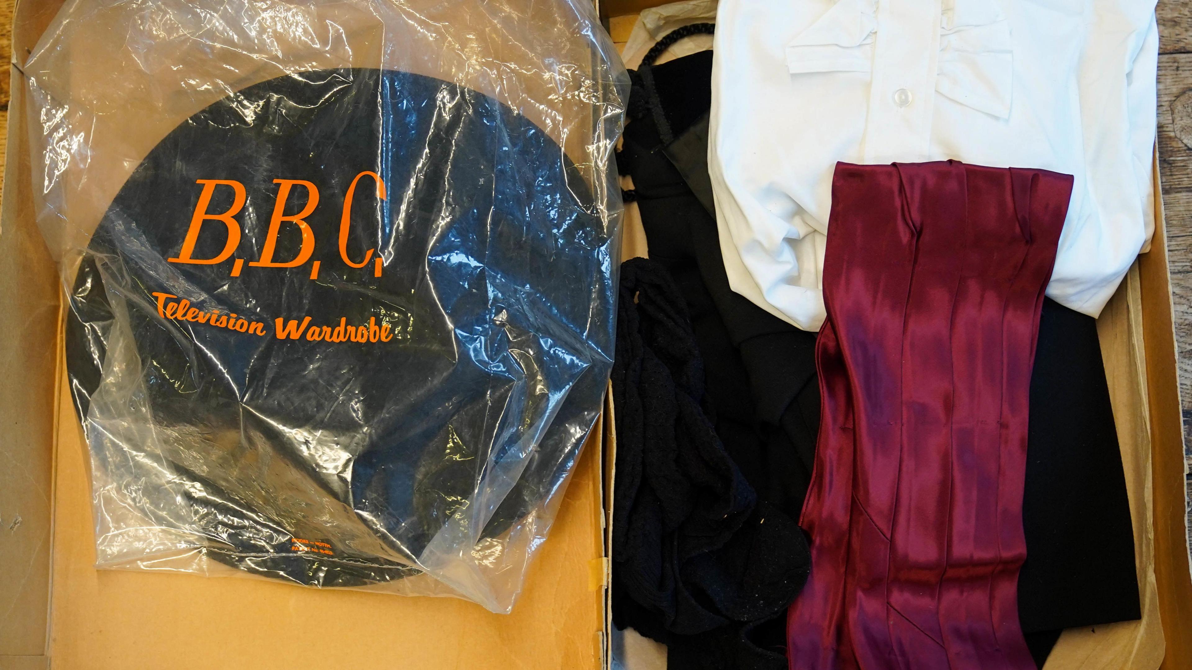 A costume box containing black, red and white clothing. Inside there is also a plastic bag with 'BBC television wardrobe' written in orange print. 