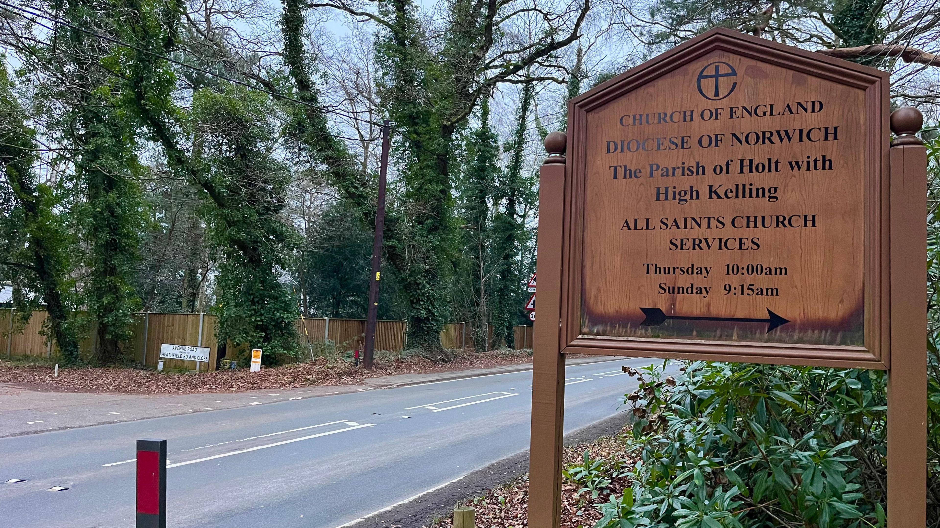 Road surrounded by trees and shrubbery with a wooden sign indicating a church.