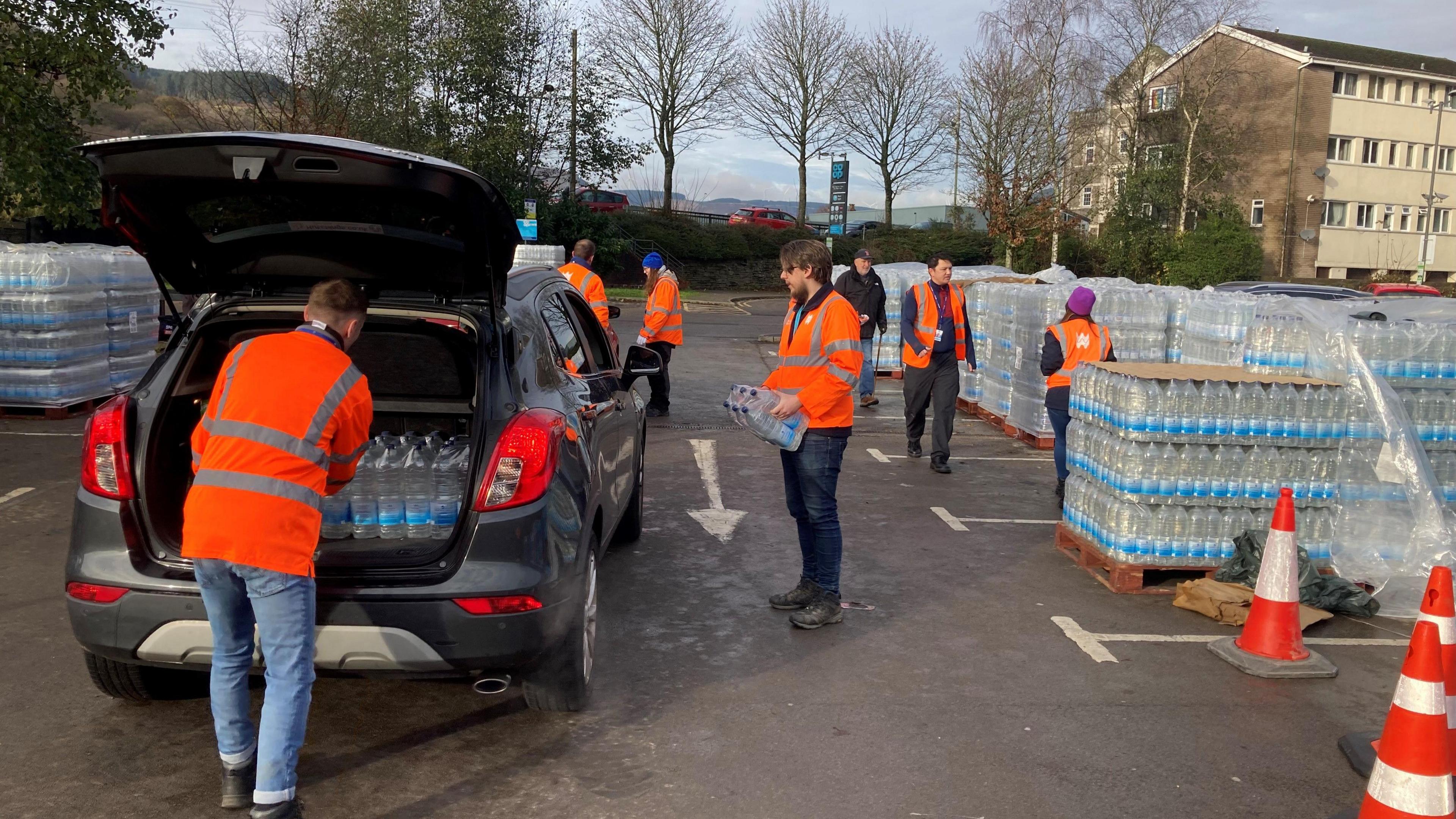 Welsh Water staff in orange jackets load cars with bottled water in a supermarket car park in Treorchy.  