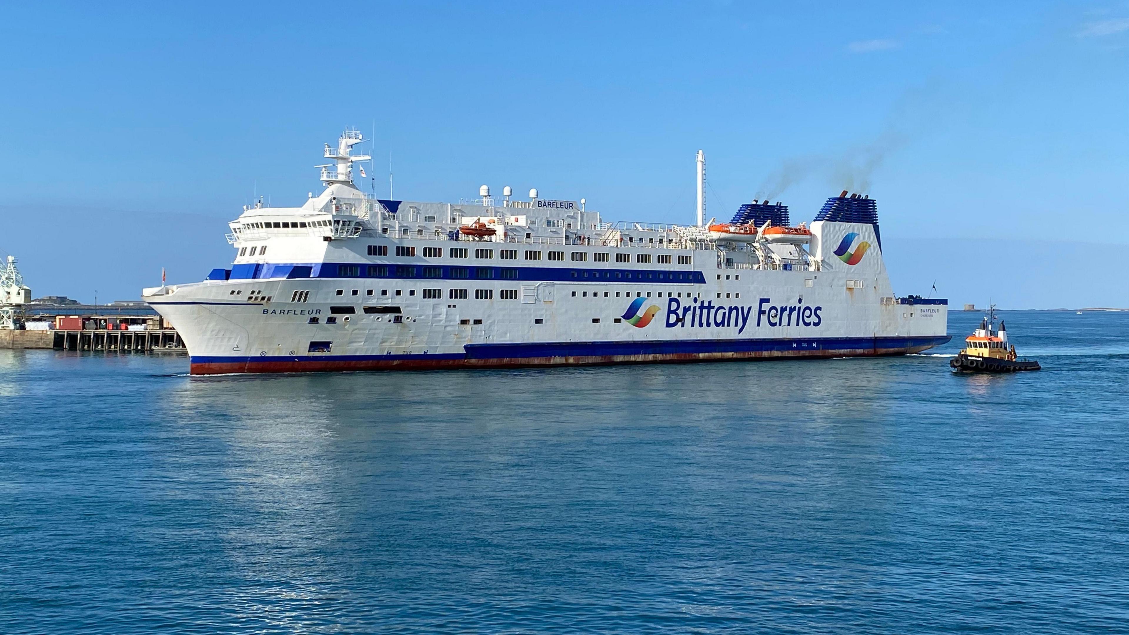 A white ferry with blue tipped chimneys with the words Brittany Ferries on the side arriving in St Peter Port Harbour.