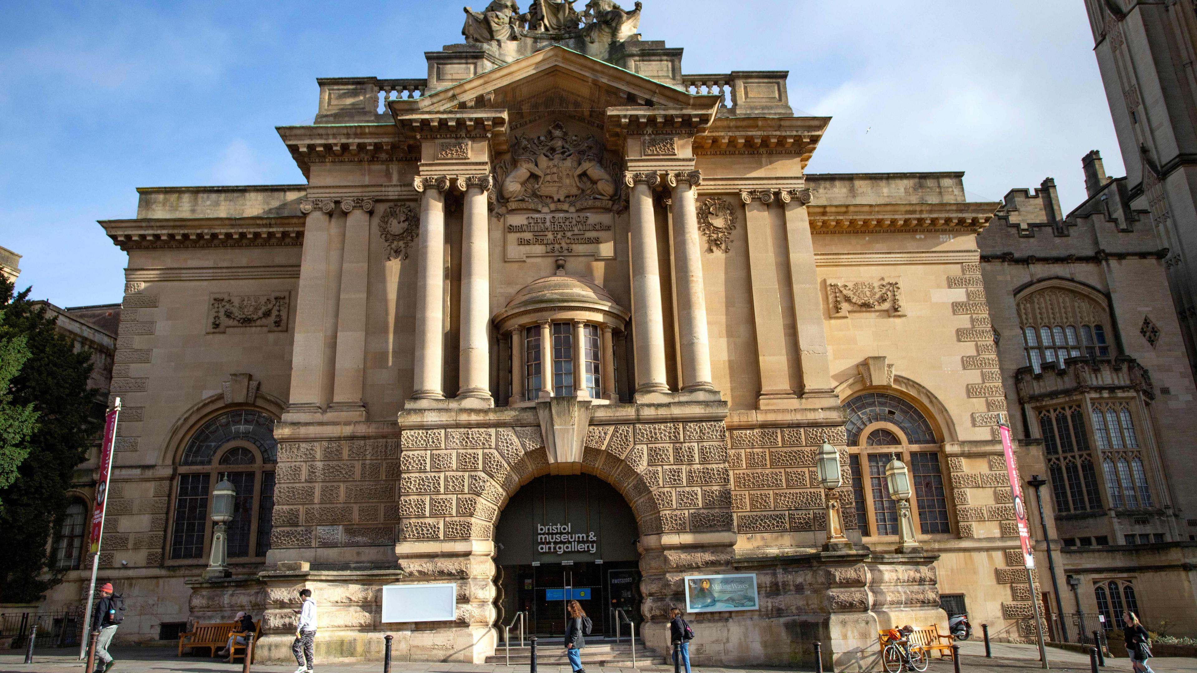 An image of a cream coloured sandstone Edwardian building,  with arched leaded light windows, and arched doorway with Corinthian columns decorative stonework