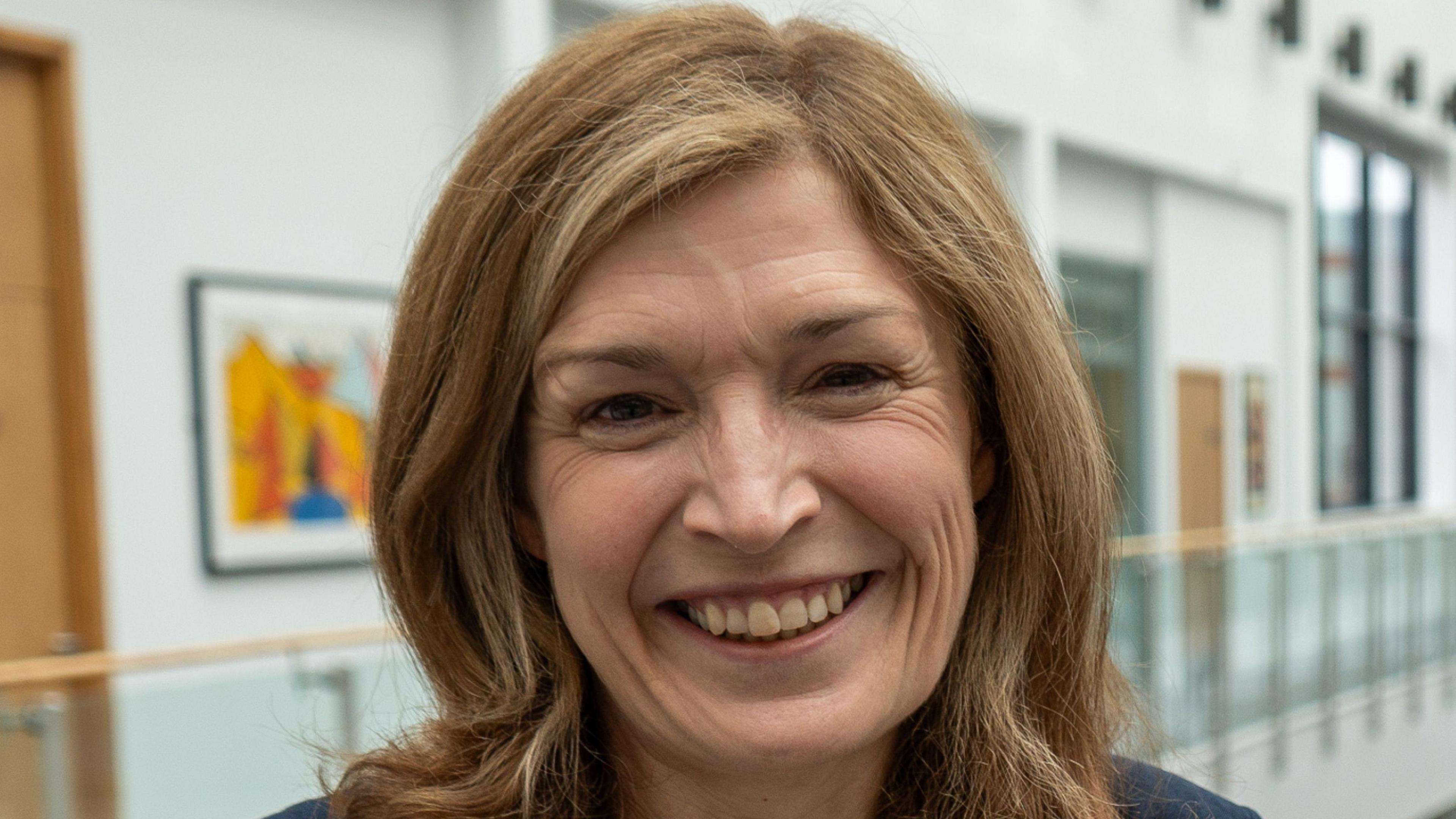 Dr Amanda Wilcox smiles and the camera. She has shoulder length brown hair.