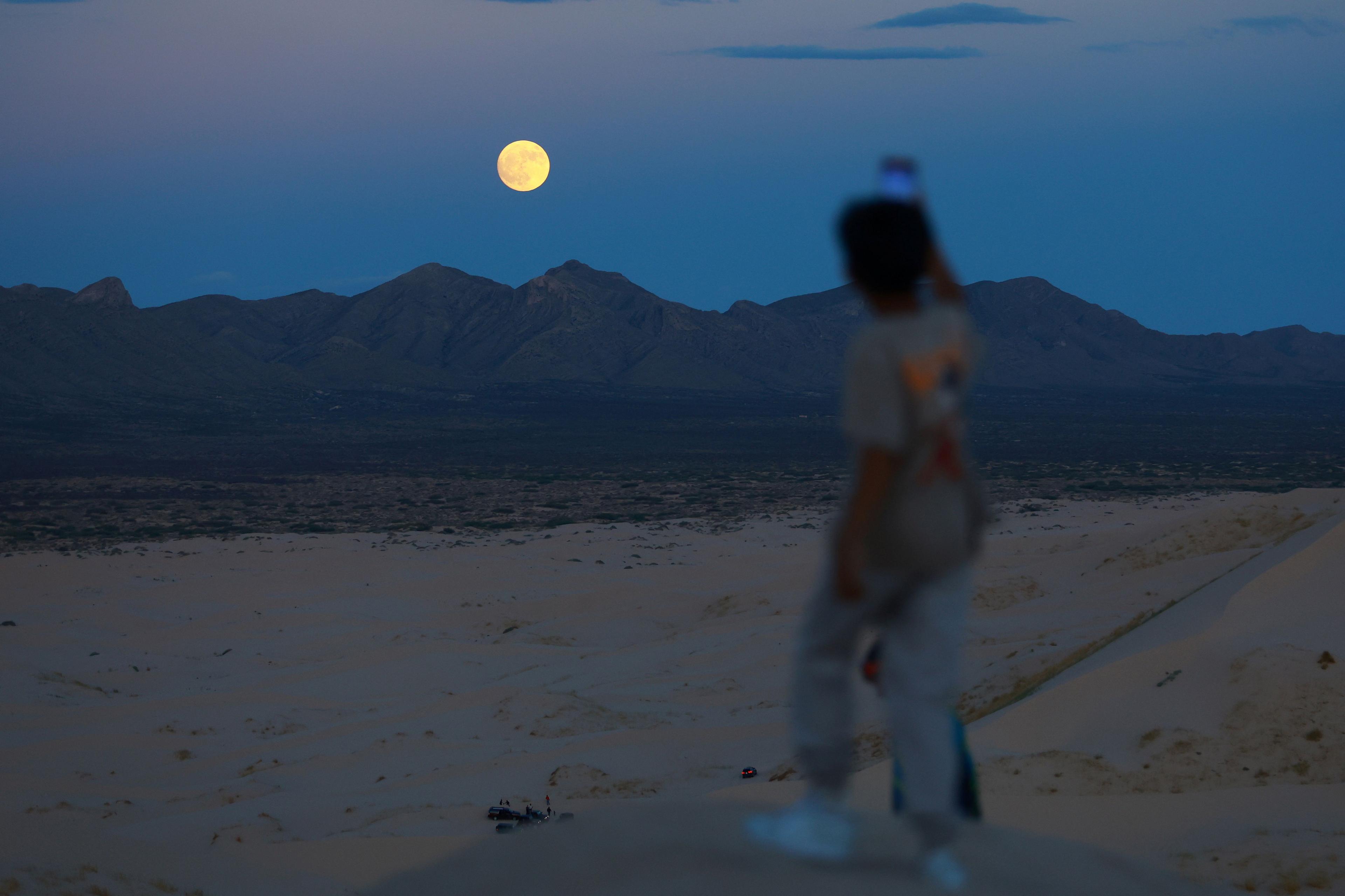 A child takes a photograph of the moon while visiting the Samalayuca dunes in the Chihuahua desert on the outskirts of Ciudad Juarez, Mexico