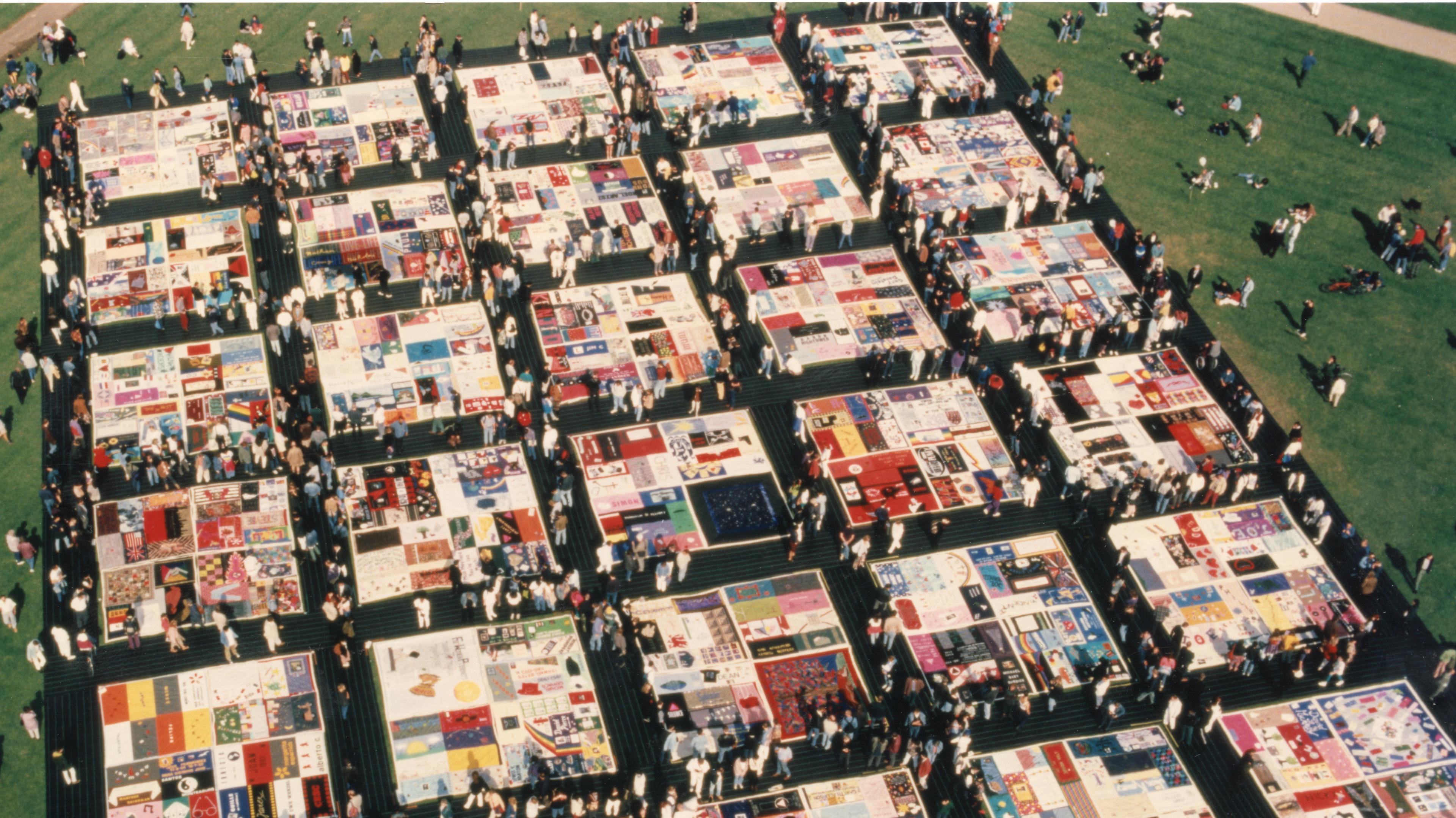 Looking down on many quilts on display on grass in a park