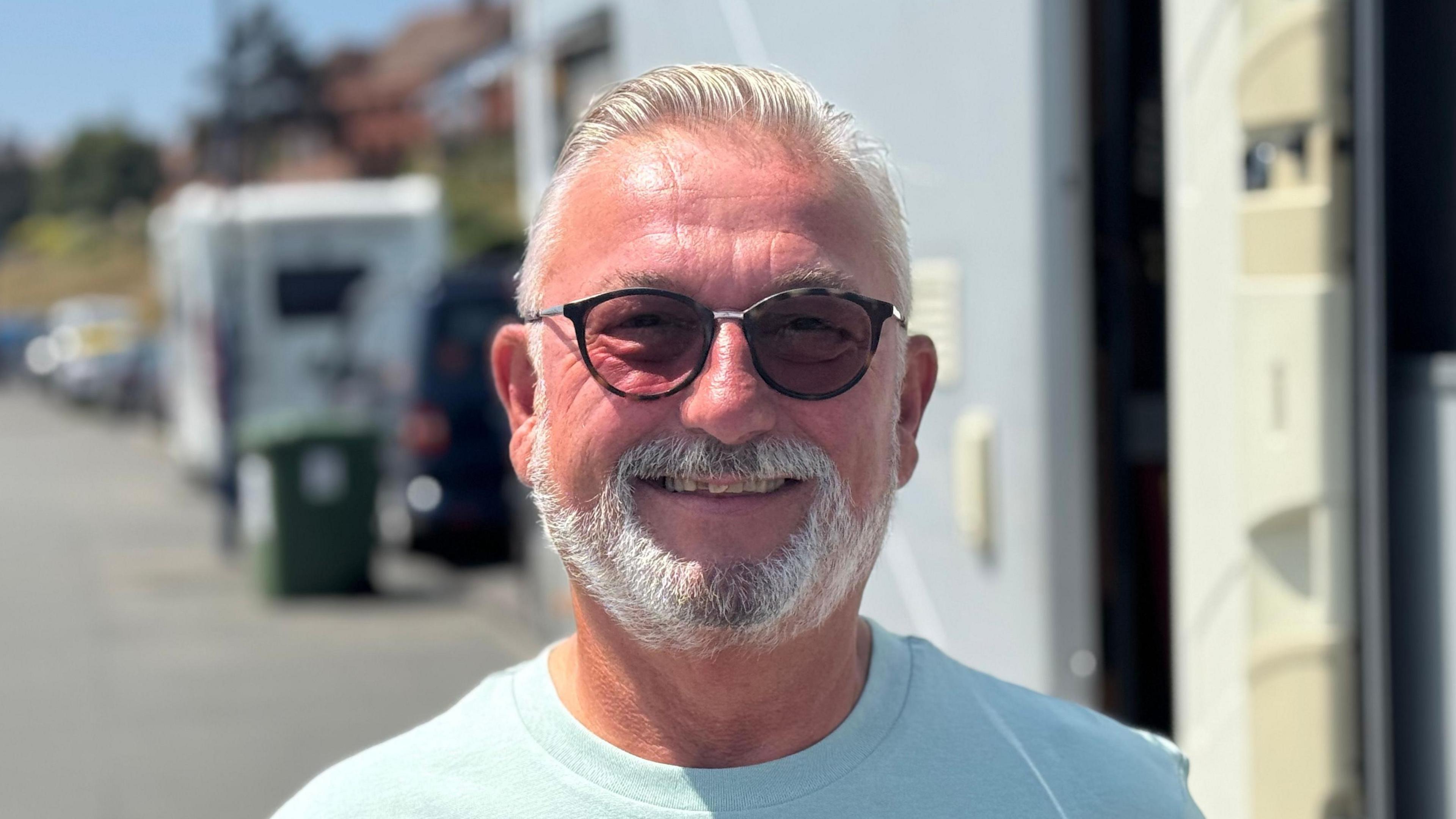 A head and shoulders shot of Ian Cable. He is smiling while looking directly into the camera. He is standing in front of his motorhome.