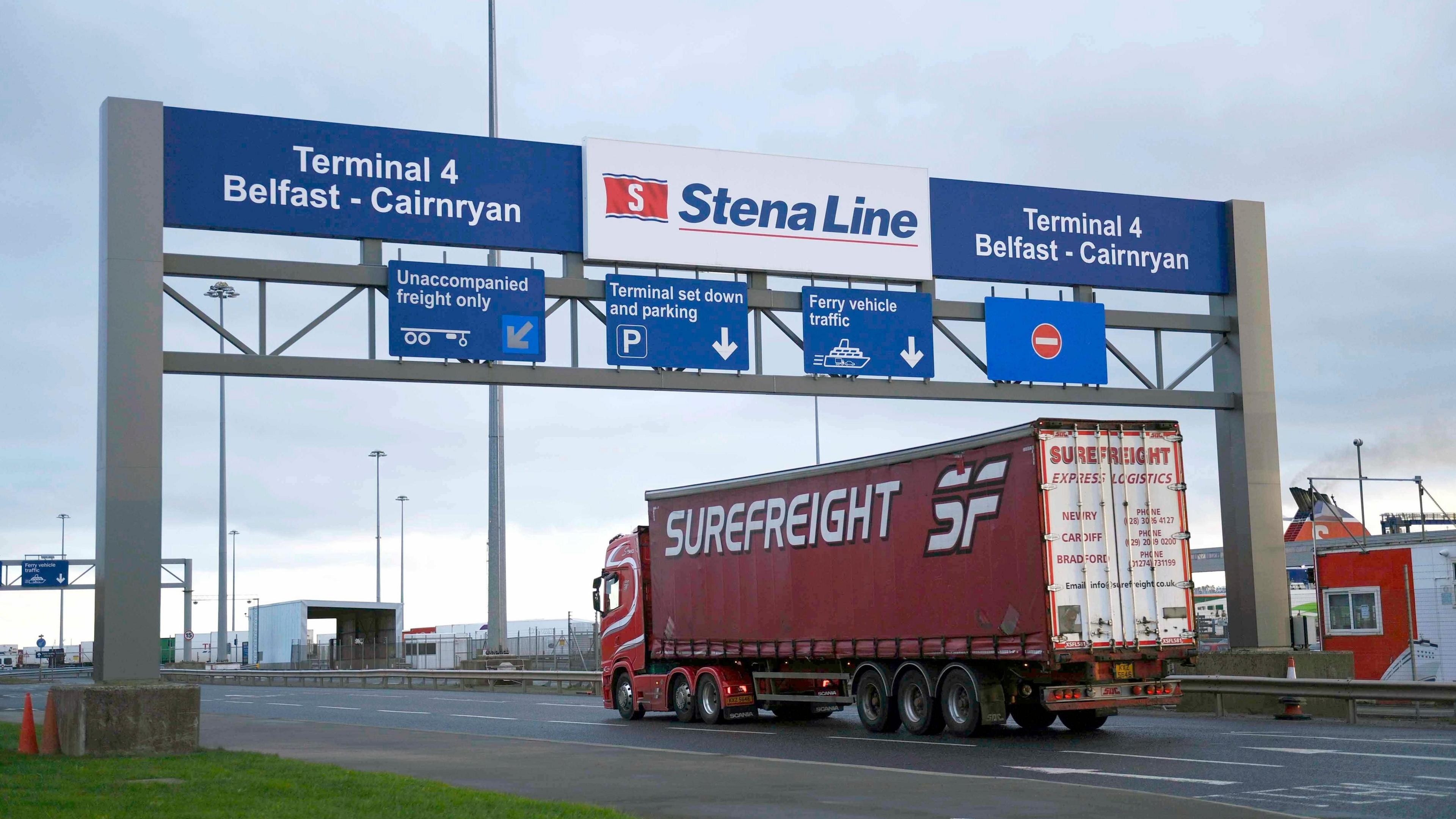 Red lorry with Superfreight logo enters gates, with blue Terminal 4 Belfast-Cairnryan sign above as well as white, red and blue Stena Line sign