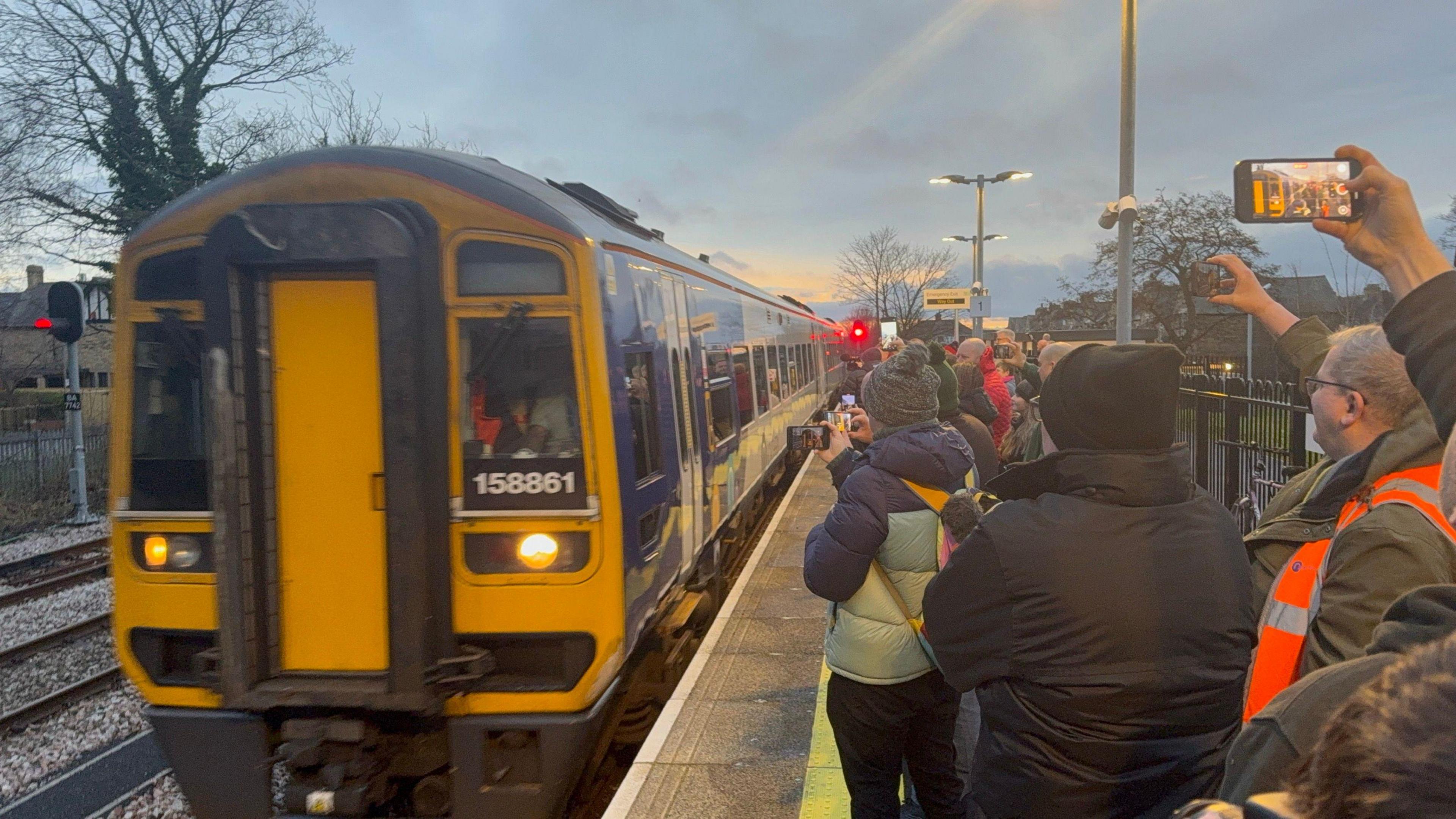 First train into platform. Lots of people on platform taking photos. 