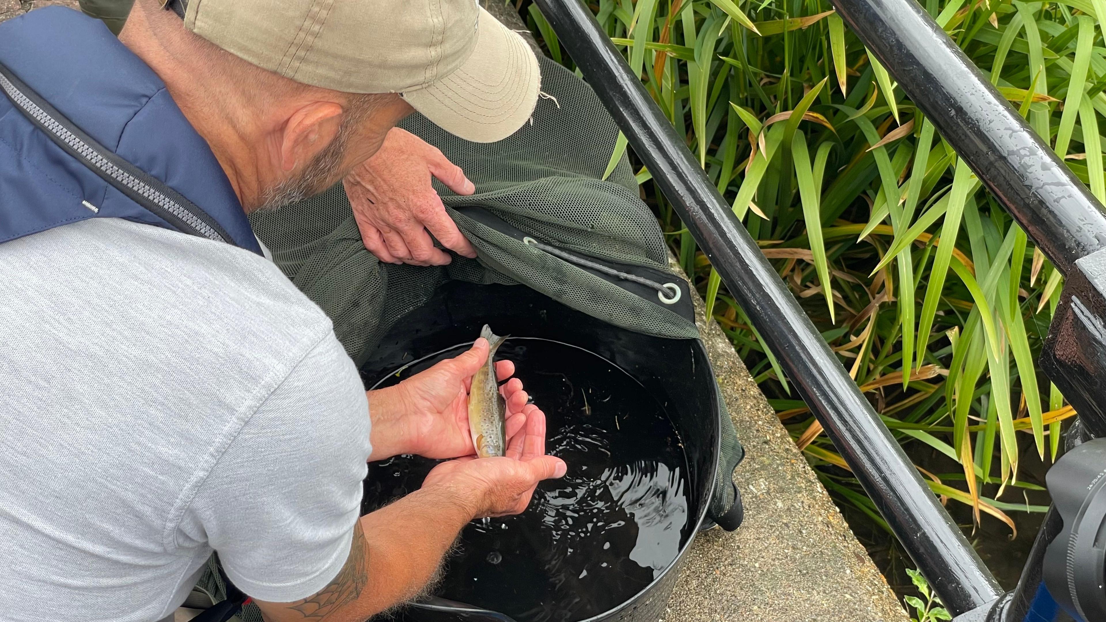 A man leaning over a bucket holding a small fish in his hands.