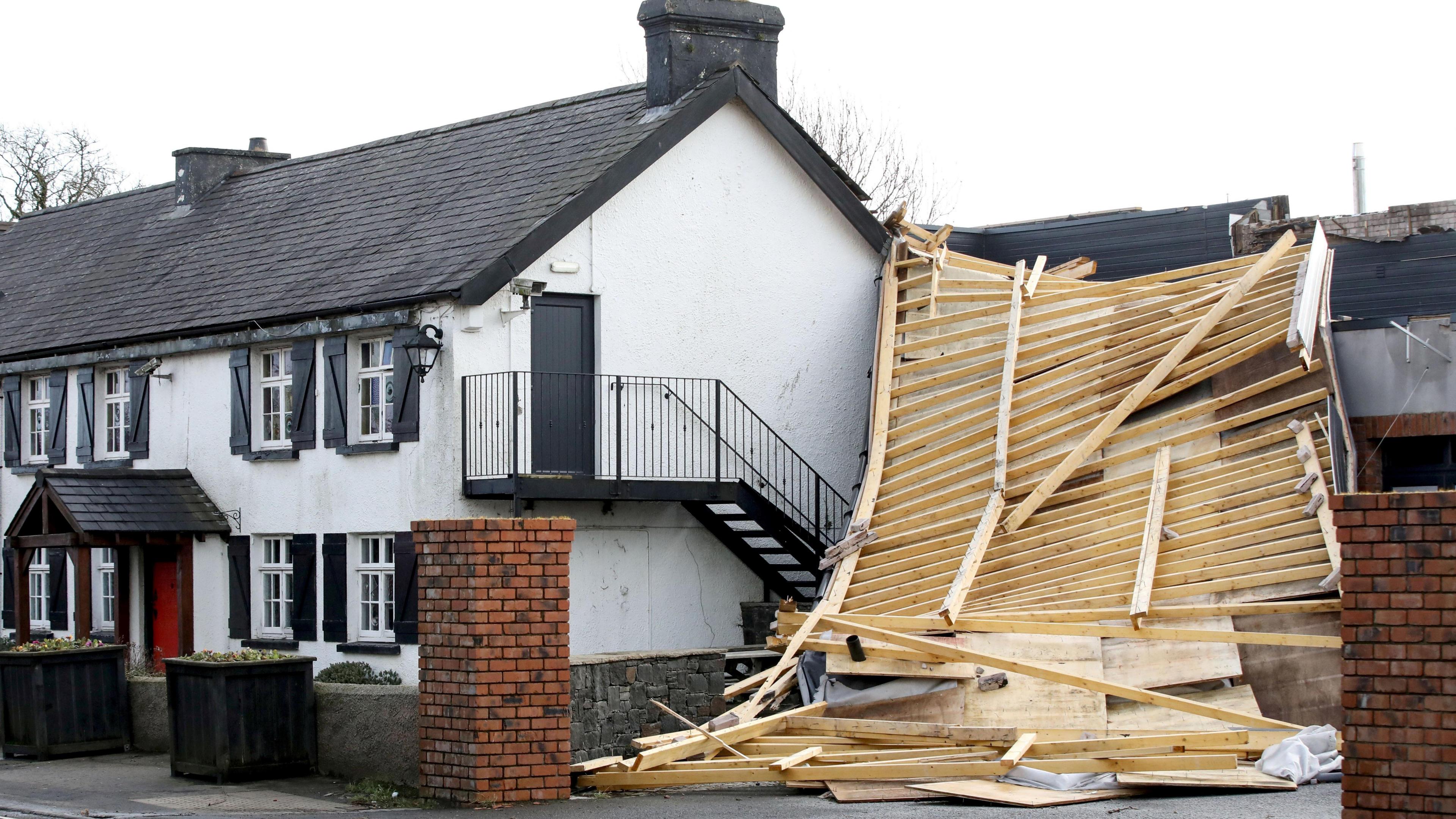 A large section of a roof hangs from a building onto the ground. Wooden beams are exposed.