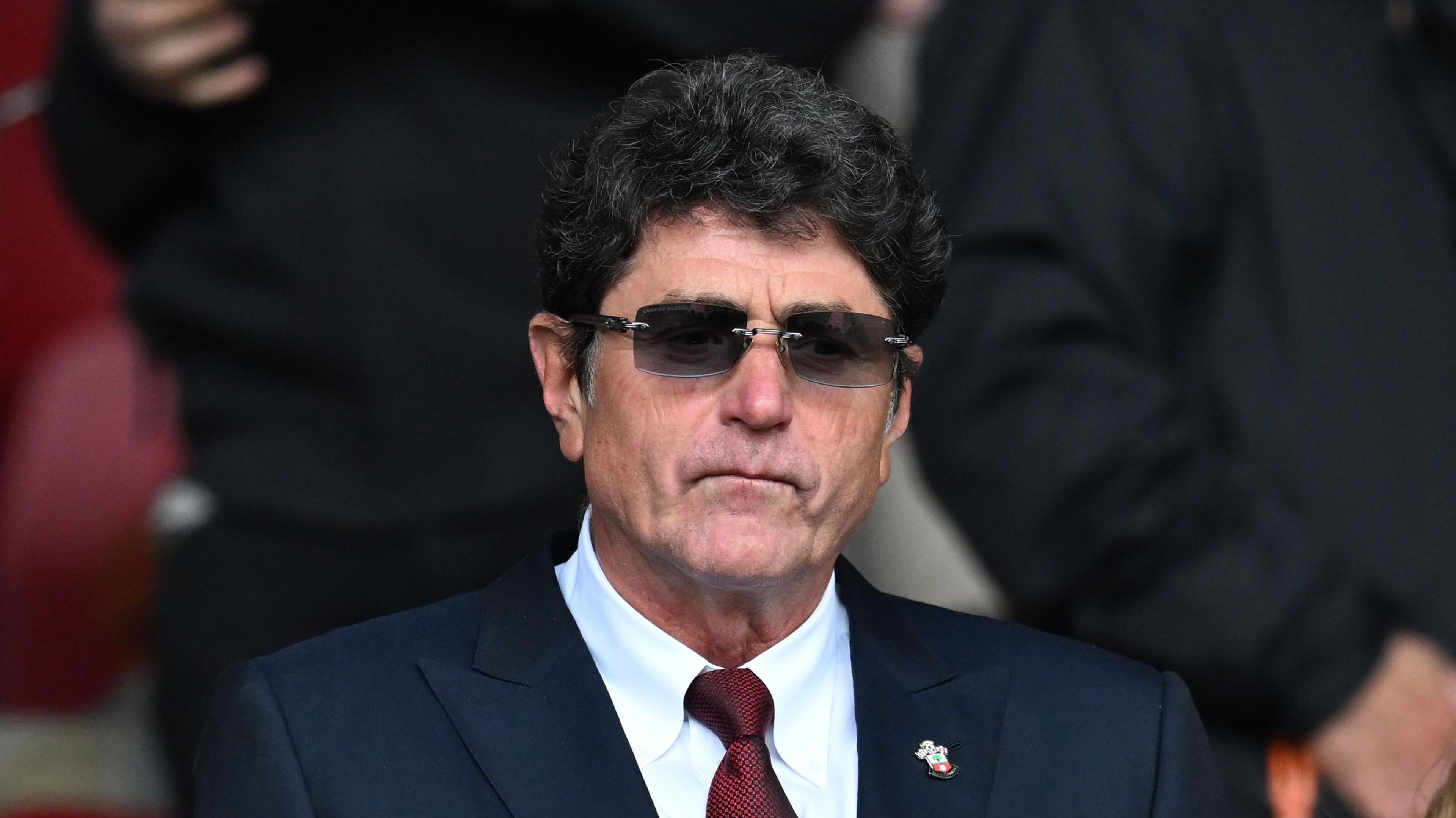 Southampton owner Dragan Solak, wearing dark glasses, a navy blue jacket and red tie, looks on at a Saints game