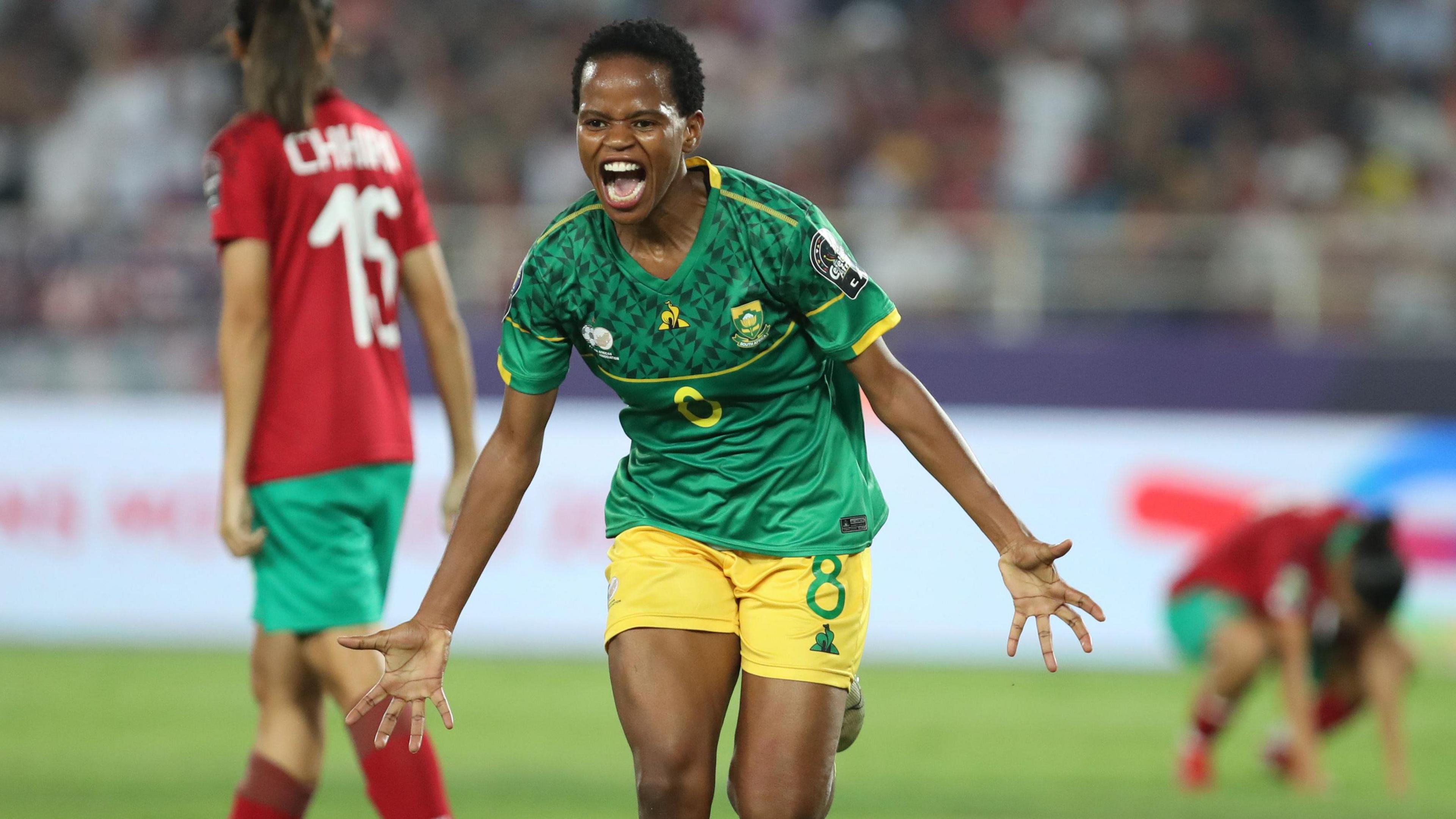 Hildah Magaia runs towards the camera with arms out to celebrate scoring for South Africa in the 2022 Women's Africa Cup of Nations final, while two out-of-focus Morocco players show disconsolate body language in the background