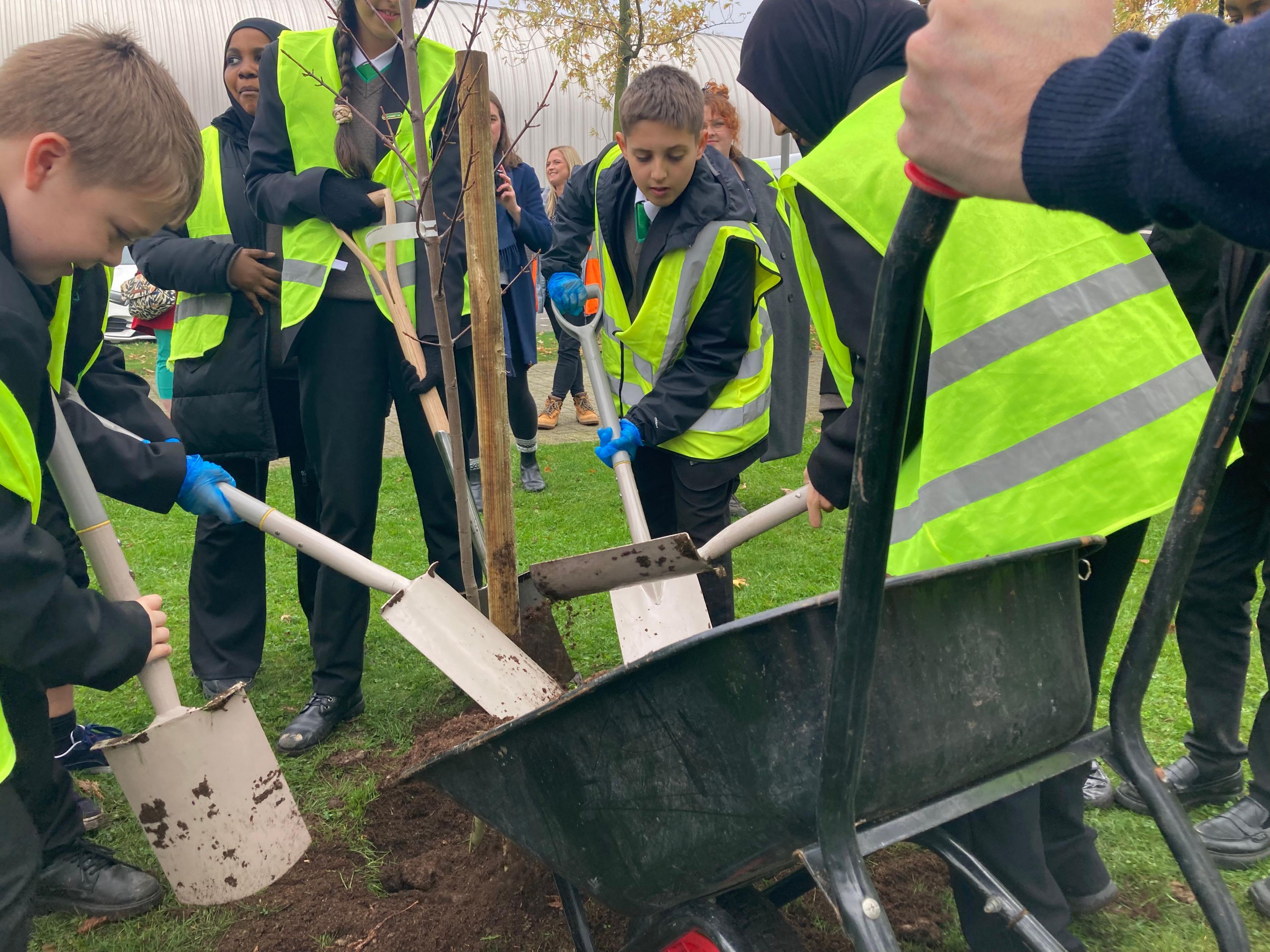 Secondary-aged school students in high-viz jackets use spades to ferry soil from a wheelbarrow