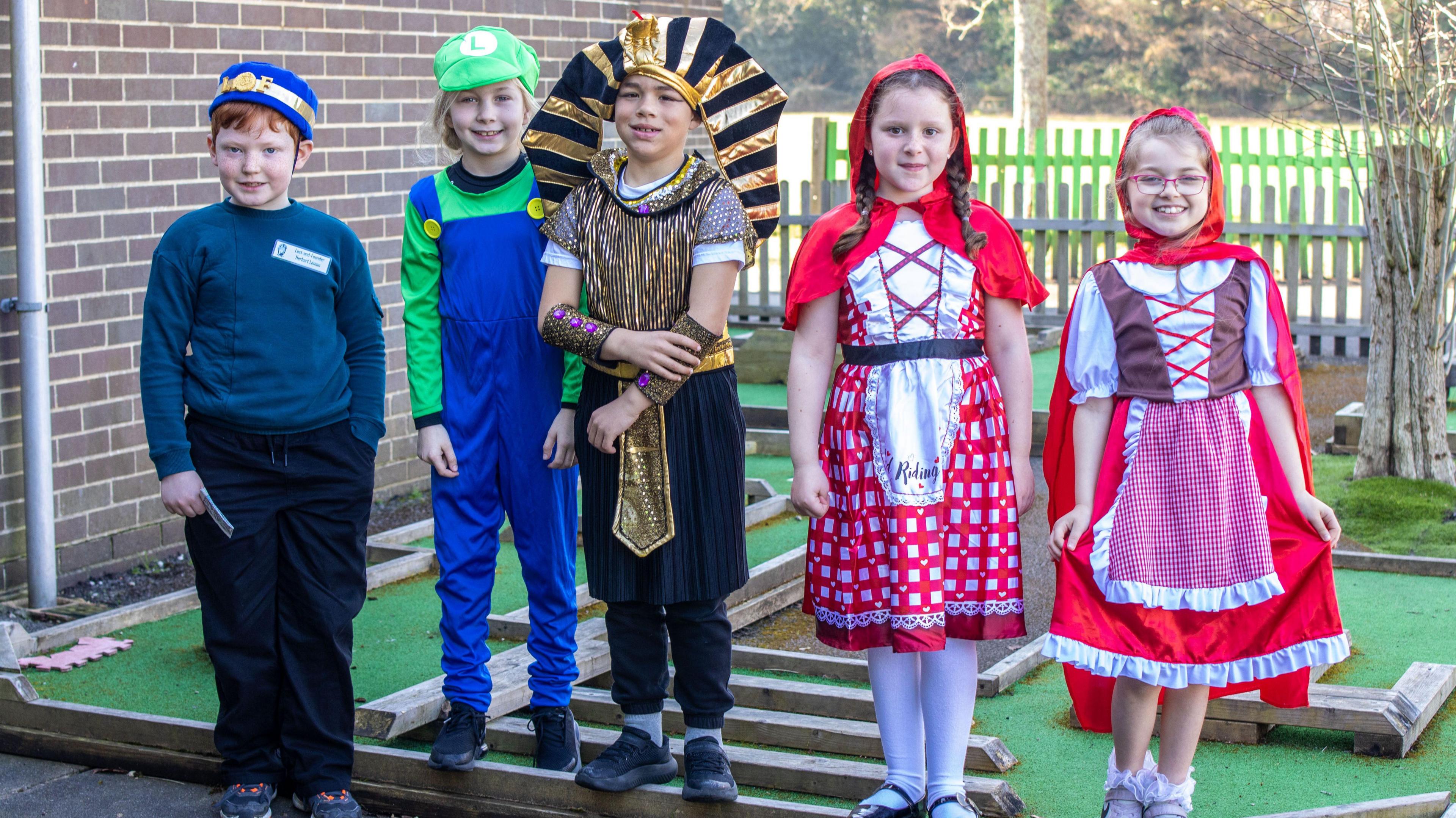 Five children dressed up as fictional characters such as the Little Red Riding Hood, a pharaoh, Luigi  and Herbert Lemon from Malamander are smiling for the camera at their school.