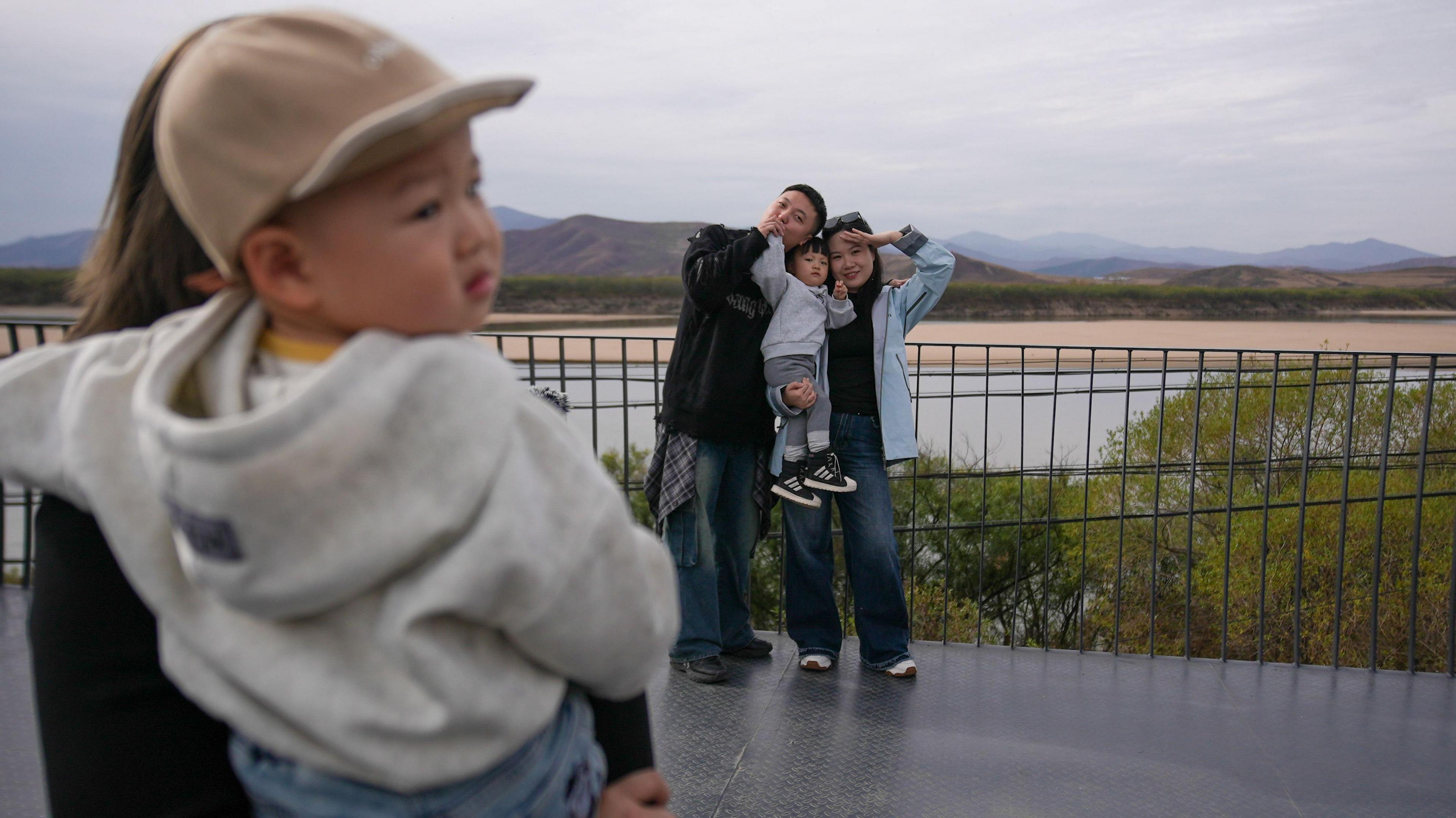 A couple with a toddler poses for photos on the building, with a view of North Korea behind them 