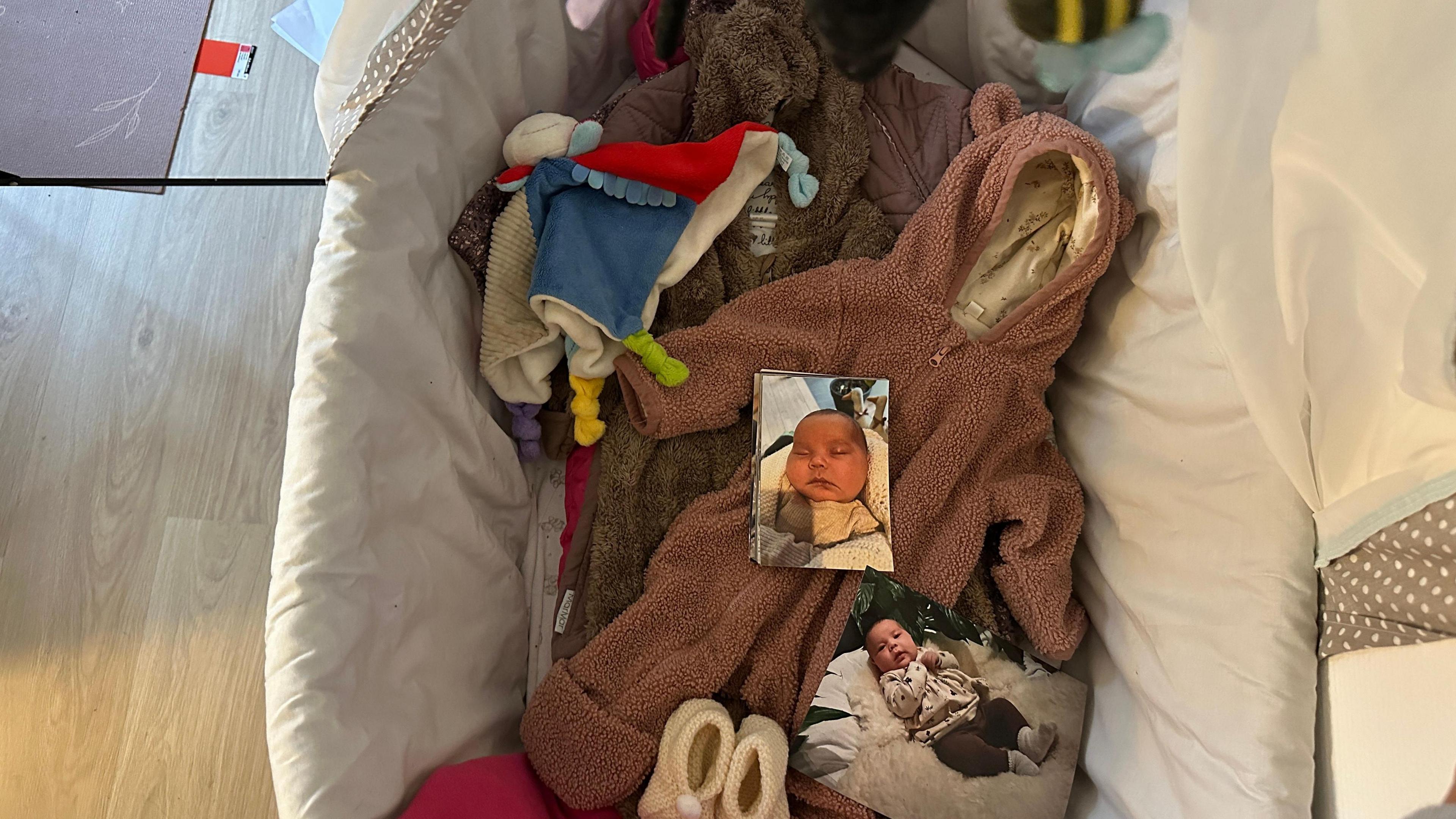 A baby cot is pictured in a room inside Keira's apartment. In the middle of the cot are baby clothes and blankets and photos of Zammi.