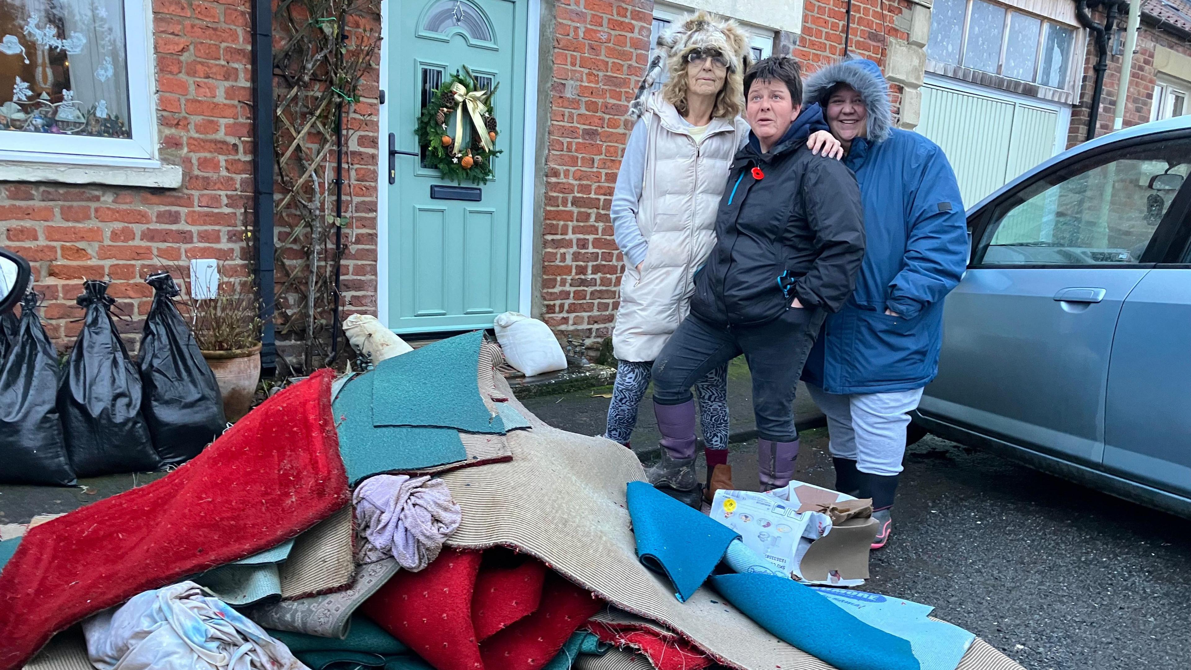 Three people outside their home which has been damaged by flooding in Kirkbymoorside - Betty Farrow, Lisa Somerville and Heidi Gibson