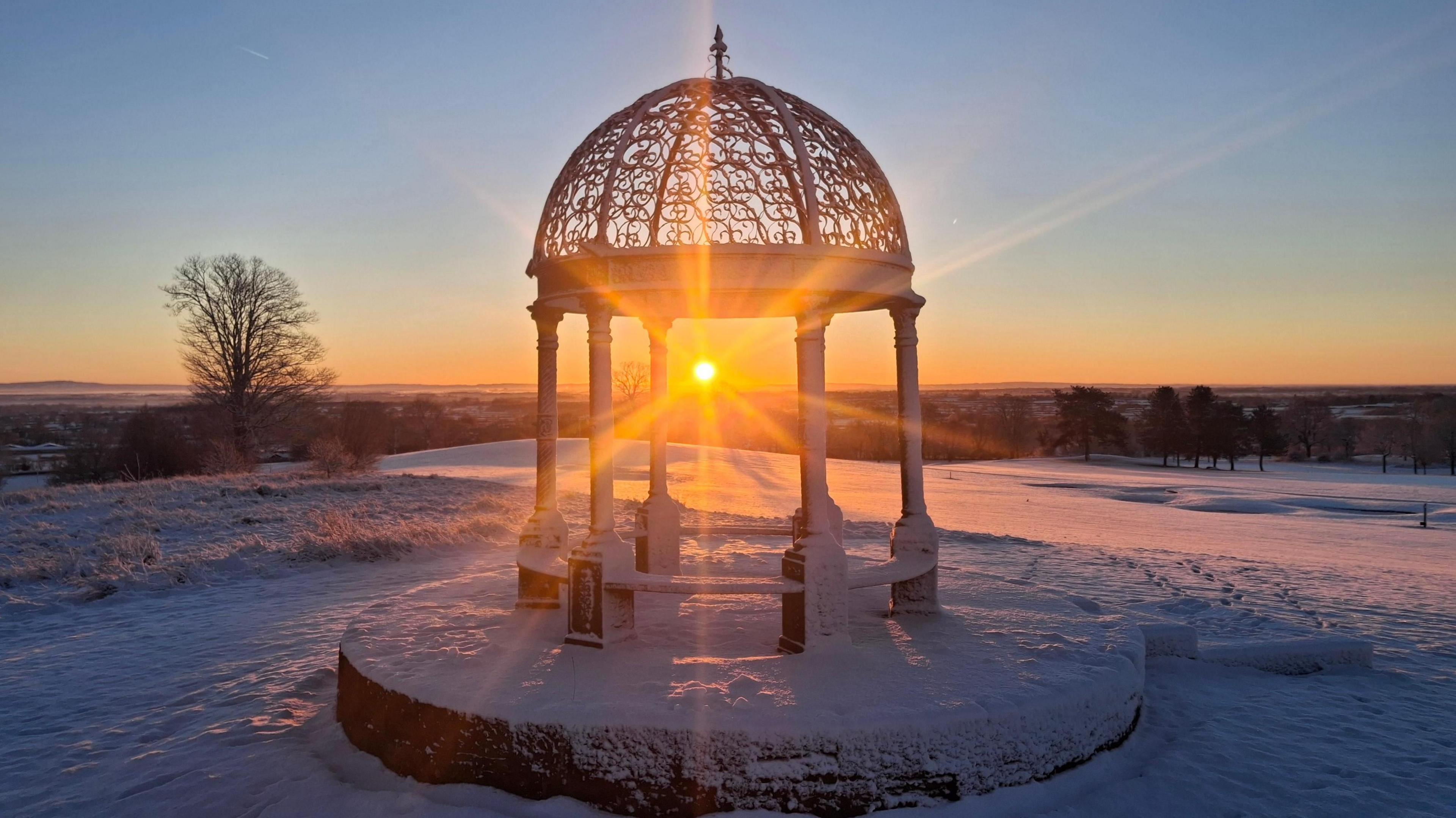 Sunrise through an iron structure, looking out over a snowy landscape
