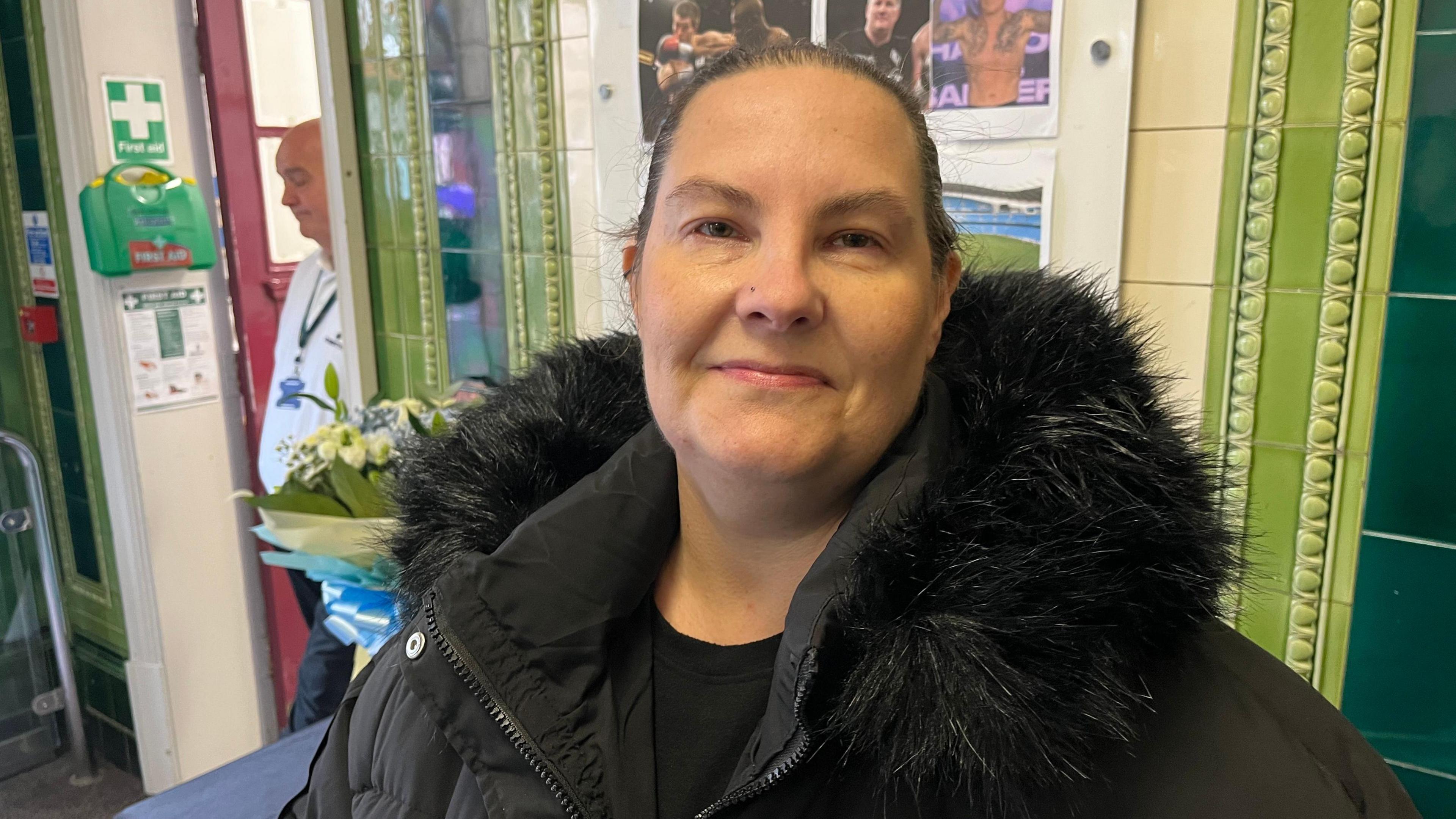 Jamie Pulford, 46, who has brown hair pulled back into a ponytail and is wearing a thick black coat with a fur hood, smiles into the camera