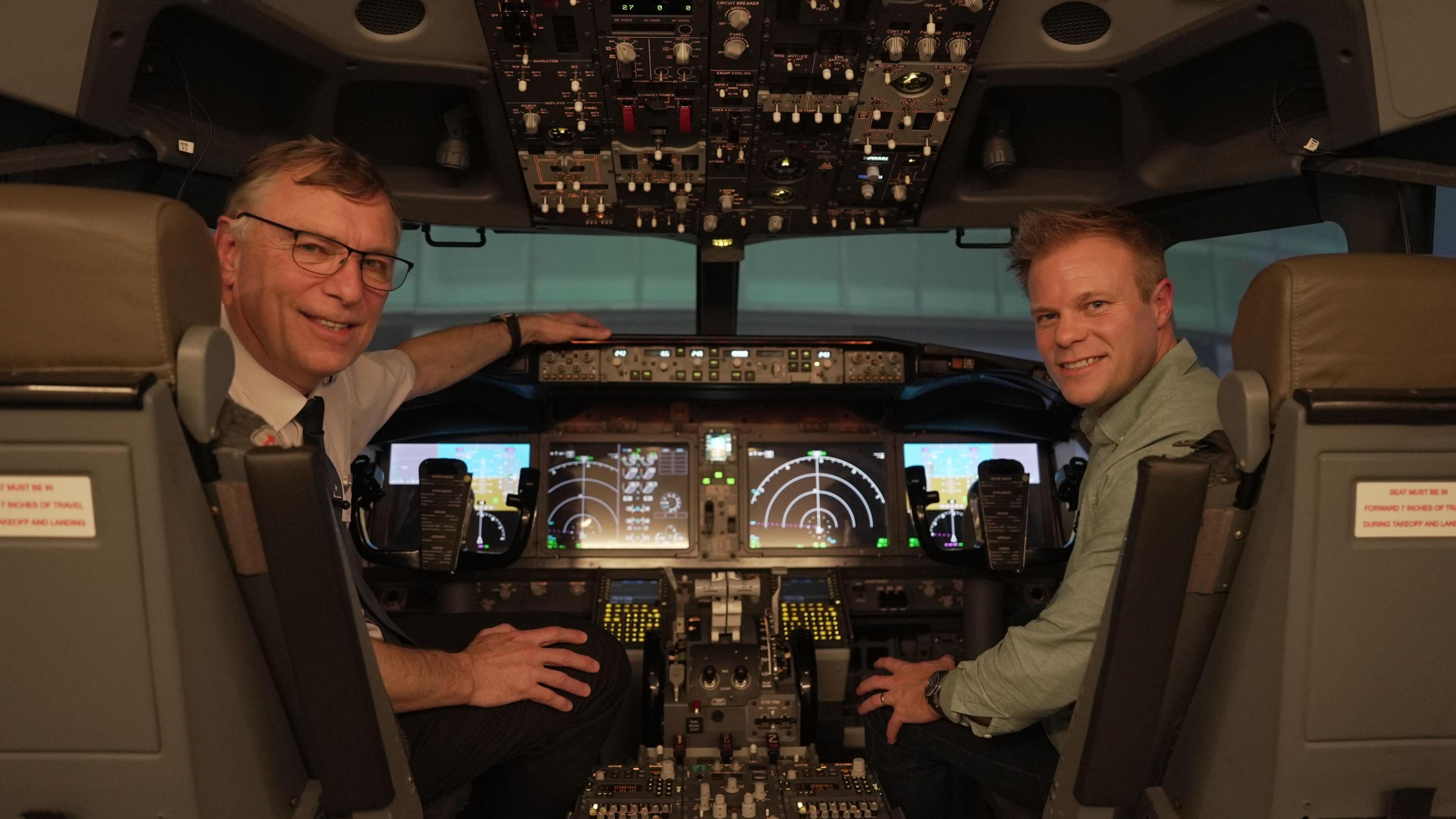 Image of the cockpit in a simulator with a pilot instructor sitting in the left hand seat with BBC Weather presenter, Simon King in the right seat.  Both are looking at the camera.