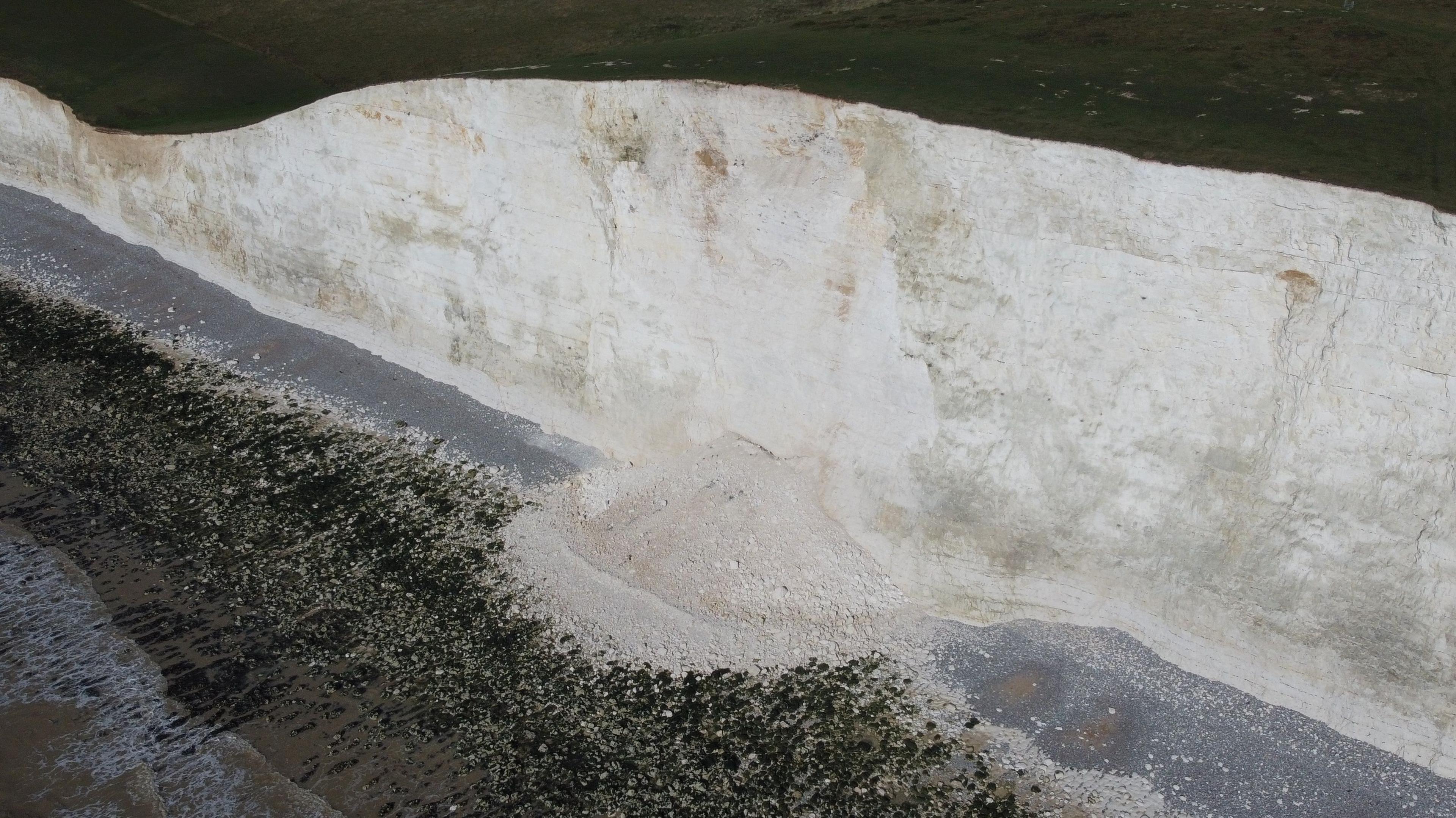 An aerial shot of the rubble from the cliff by the algae-covered floor. The white cliff is behind it with grass on top.